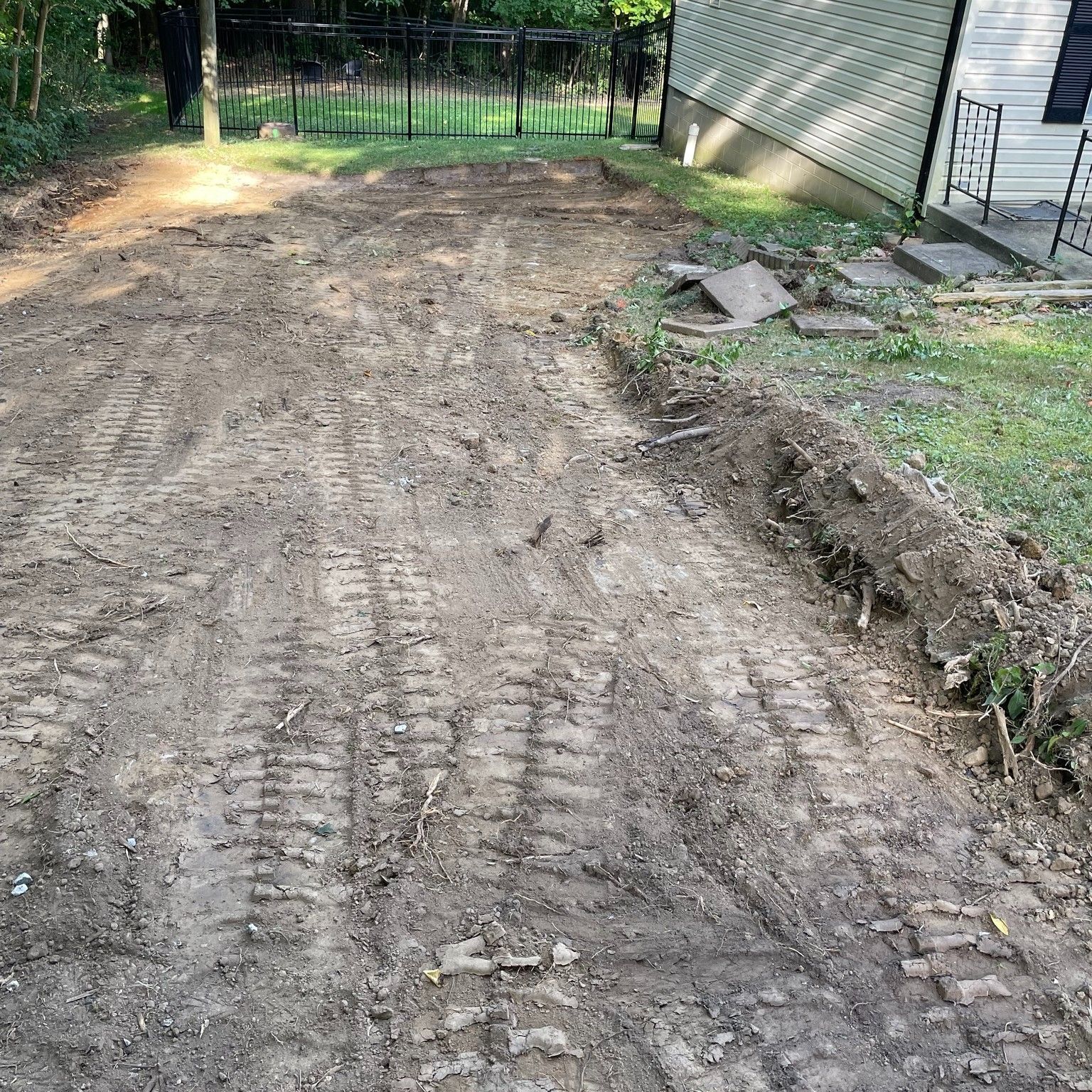 Dirt driveway or yard area with tire tracks, a shallow ditch on the right, and a fence in the background