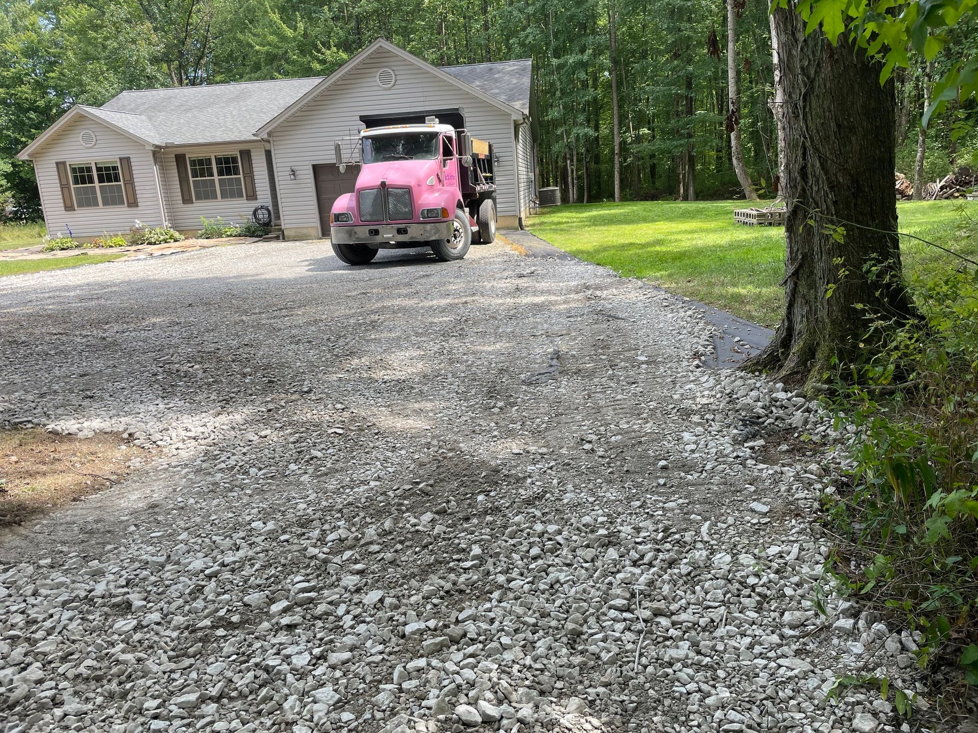 Pink Jeep parked on a gravel driveway in front of a house surrounded by trees