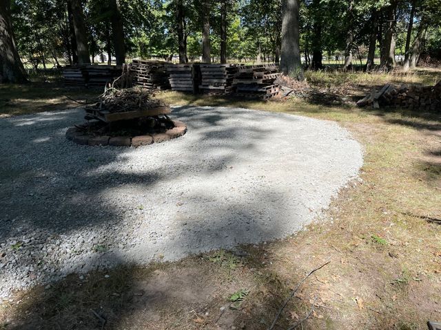 Gravel clearing with a fire pit and wooden benches in a wooded park area
