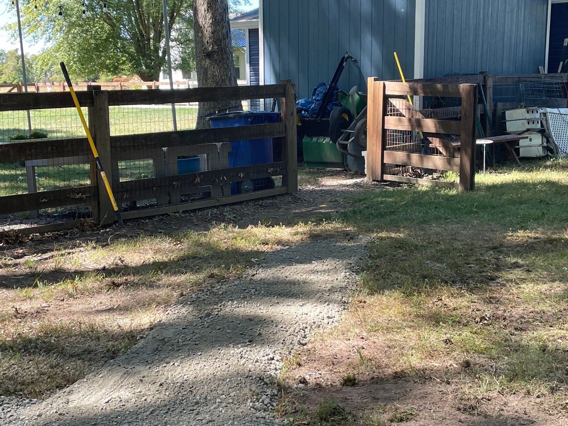 Wooden pallet fence and blue shed in a grassy yard with a dirt path in the foreground