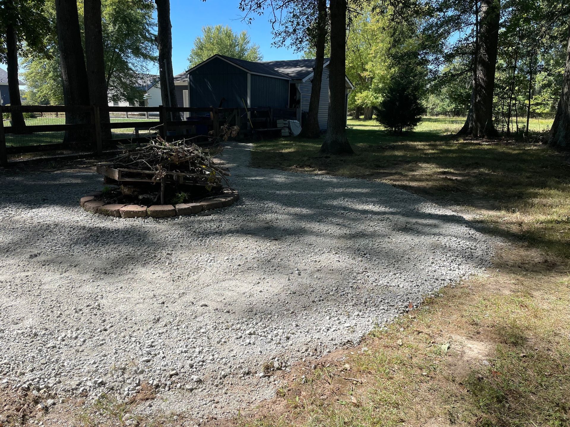 Gravel campsite with a fire pit, picnic tables, and a small cabin among trees in daylight