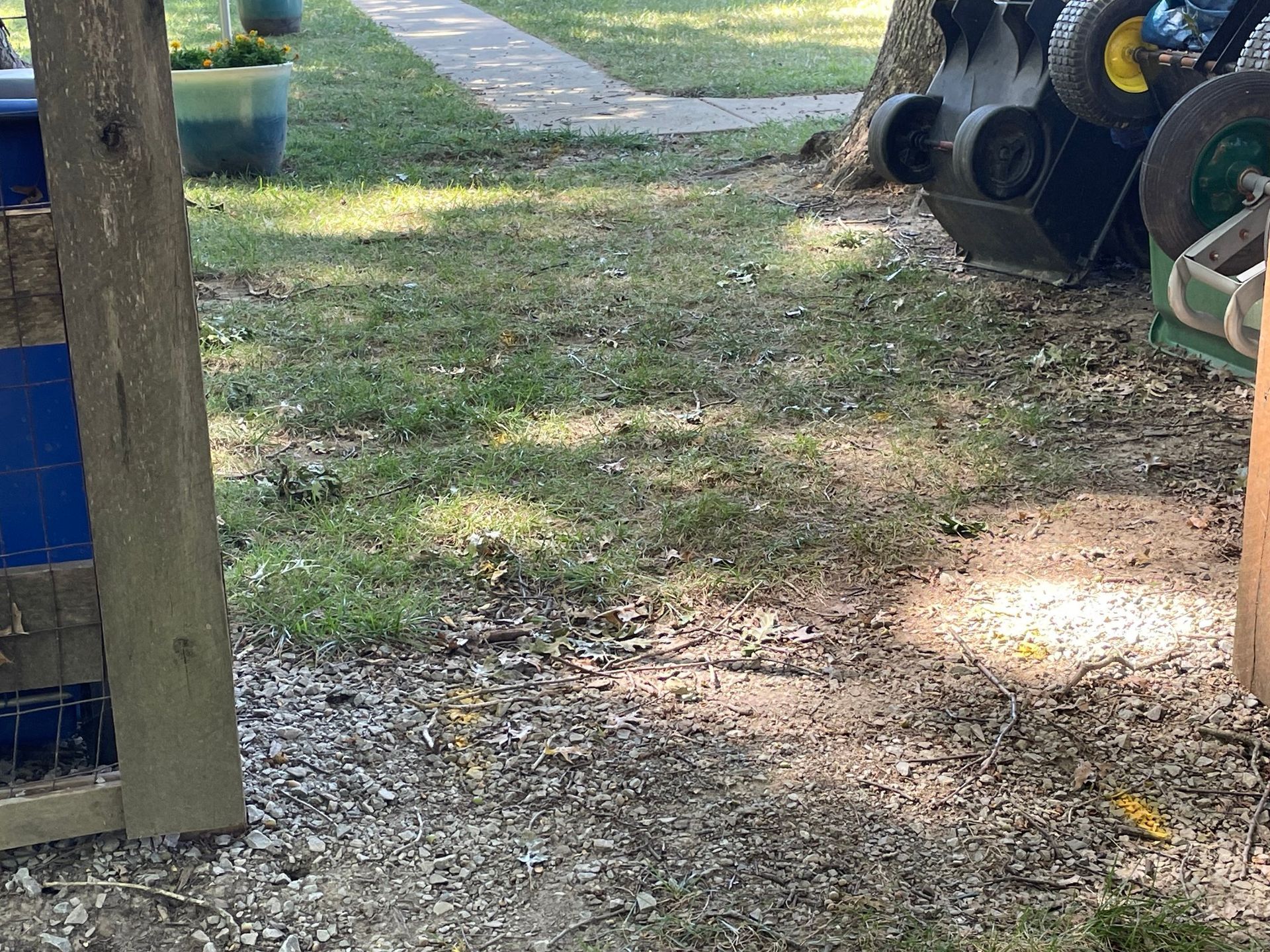 Gravel path through a grassy yard with scattered playground equipment and a wooden fence.