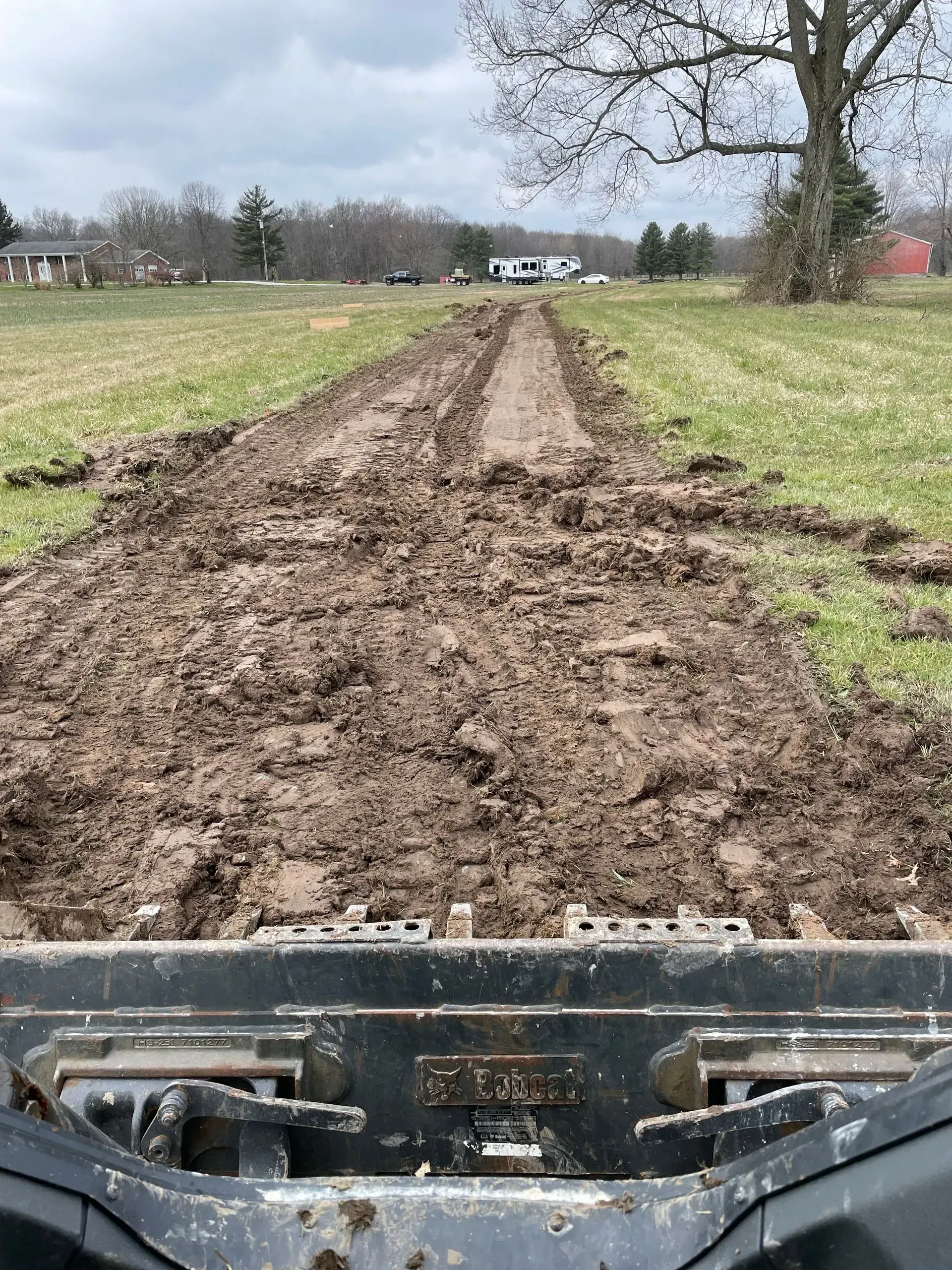 Rough muddy track through a grassy field, seen from a vehicle under a cloudy sky.