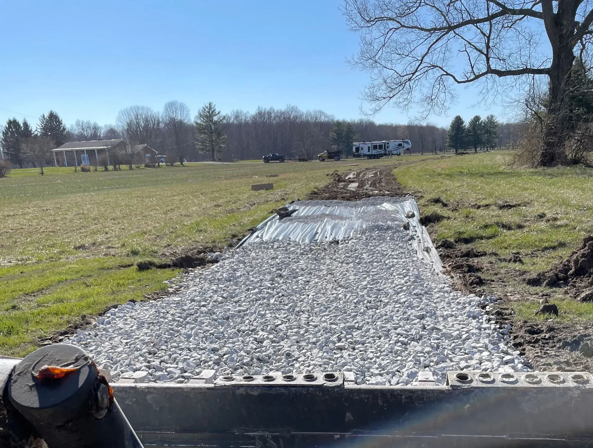 Gravel path laid through a grassy field under a clear blue sky, with trees in the distance.