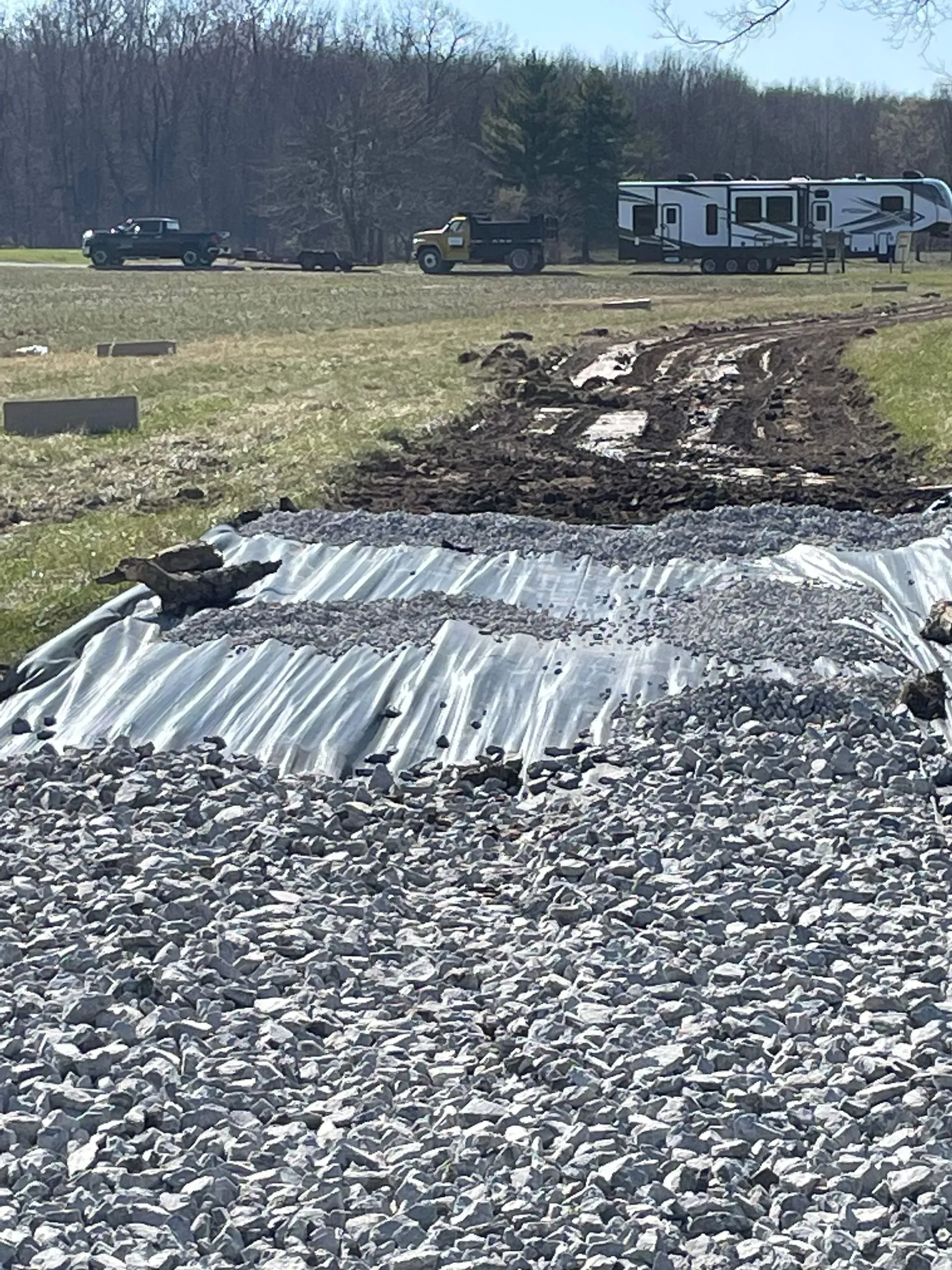 Gravel-covered erosion control area with muddy tire tracks and parked vehicles near a camper in the background