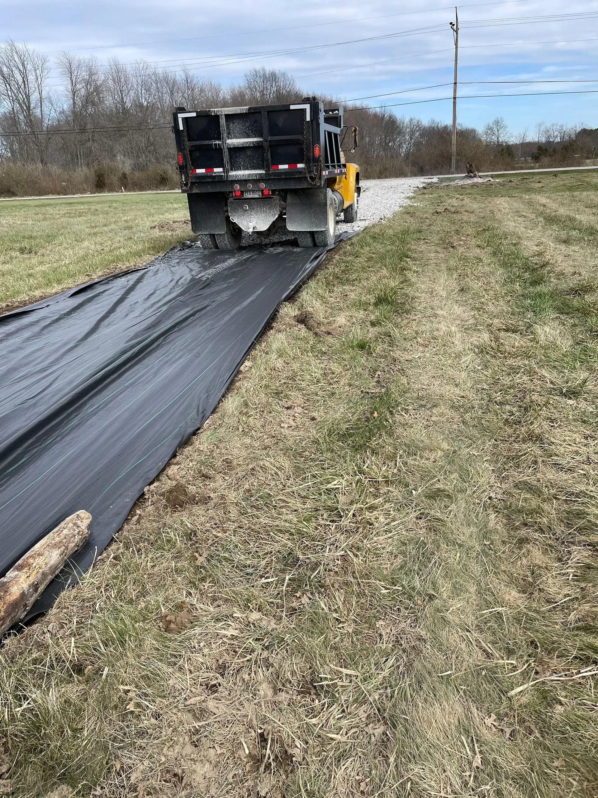 Worker laying black landscape fabric along a grassy roadside field
