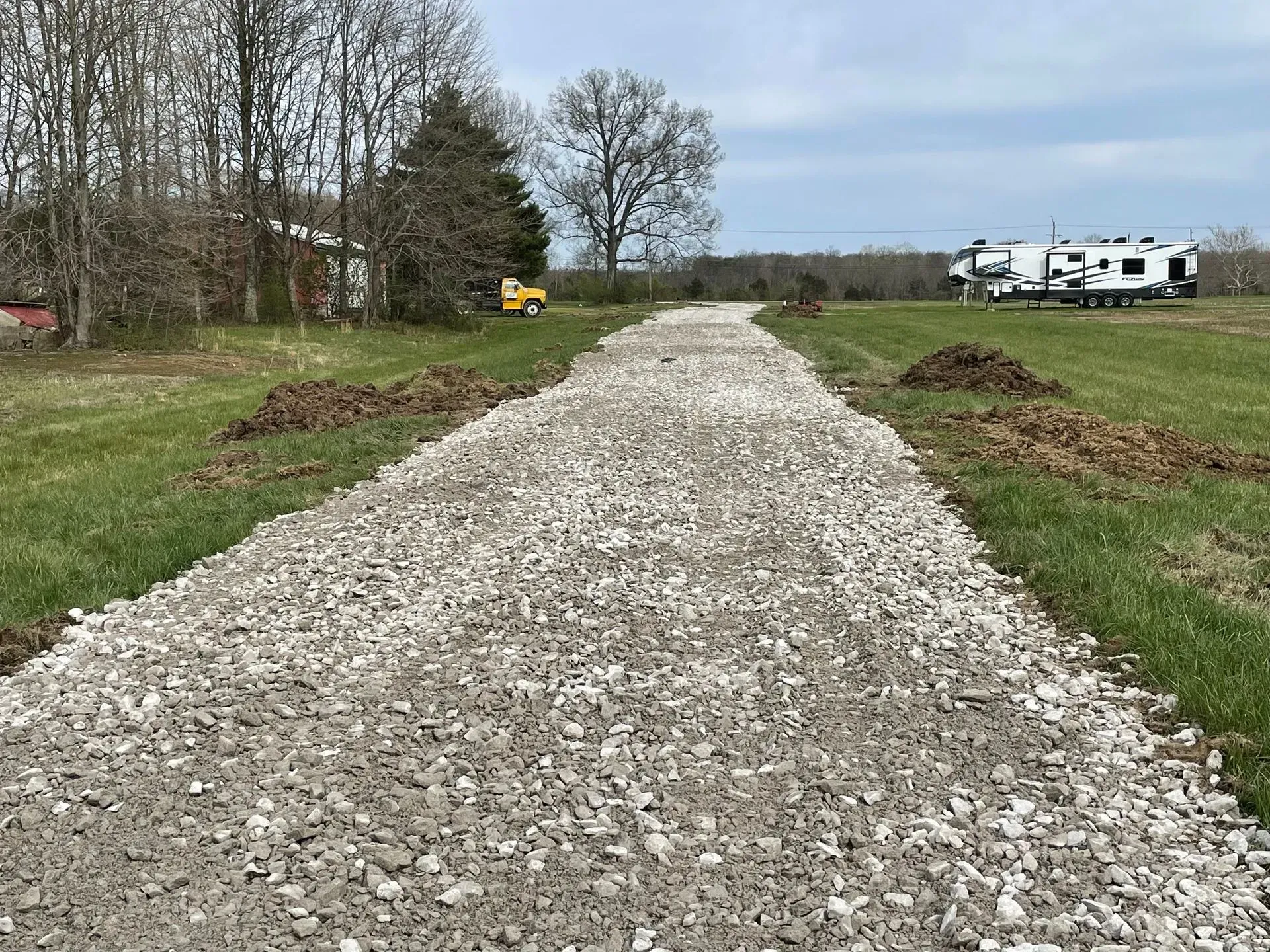 Gravel path through grassy field with trees, small yellow vehicle, and white RVs in the distance.