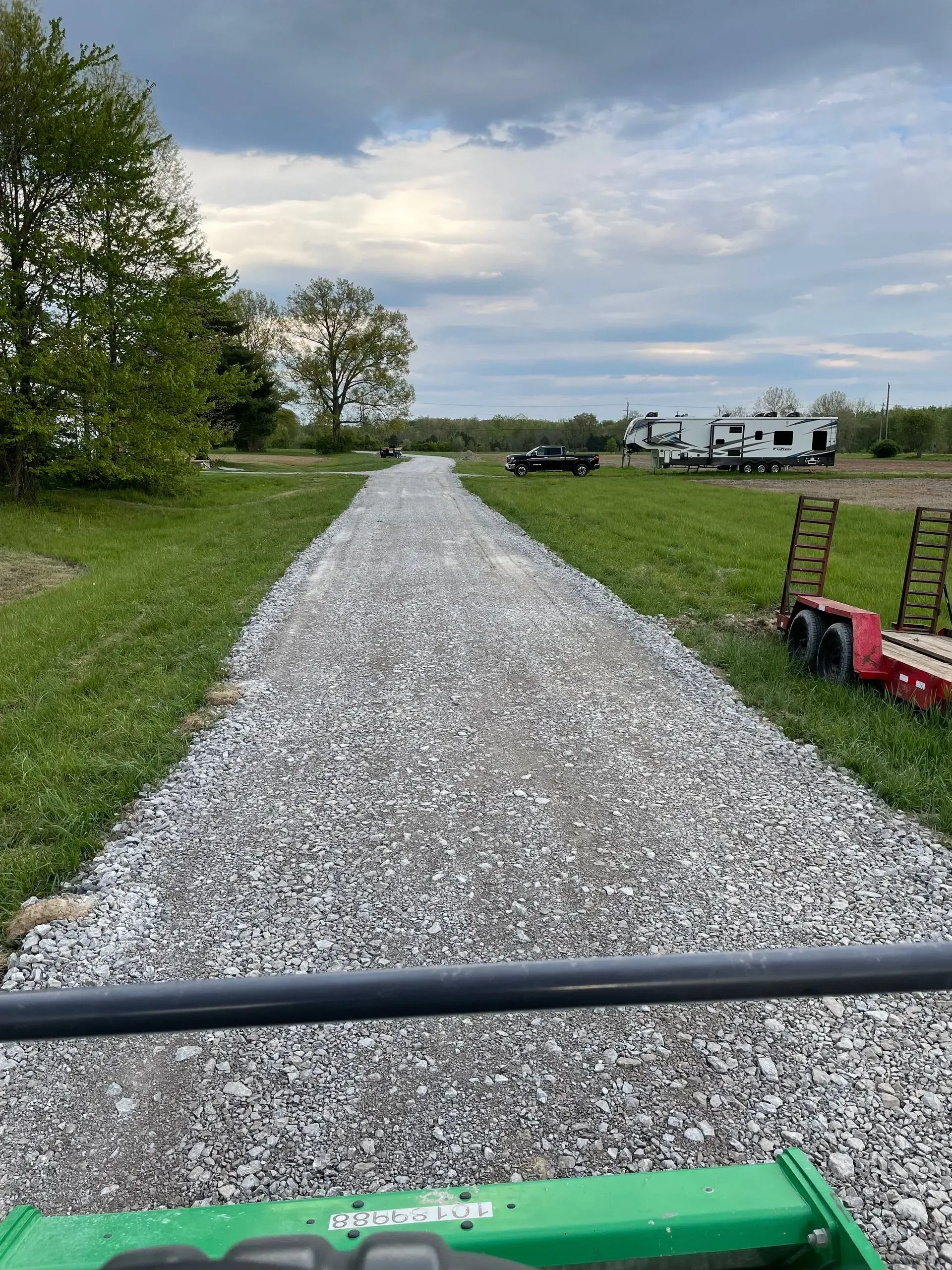 Gravel driveway leading to a grassy RV campsite with trees and parked campers under a cloudy sky