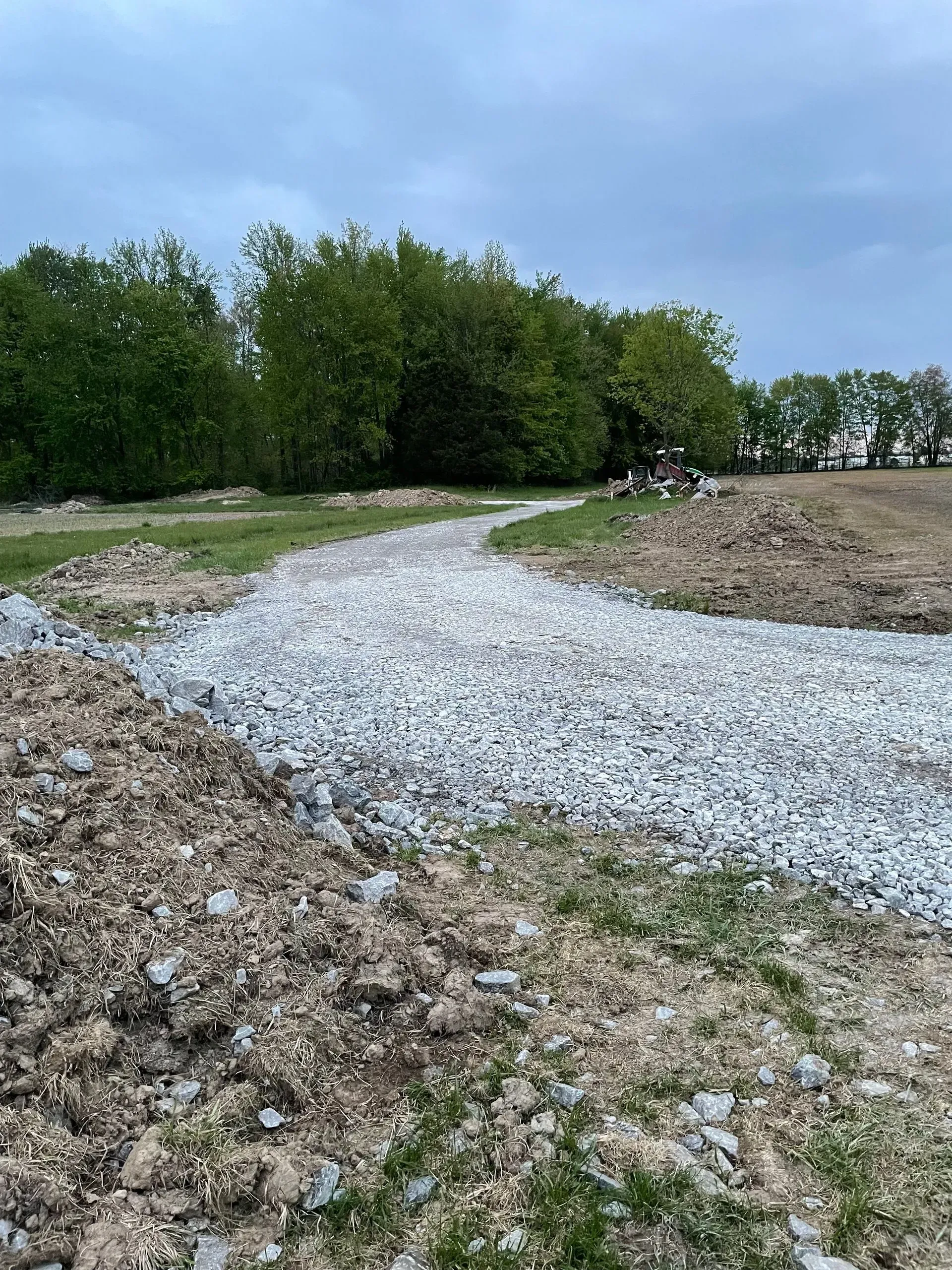 Gravel path curving through a grassy field with trees under a cloudy sky
