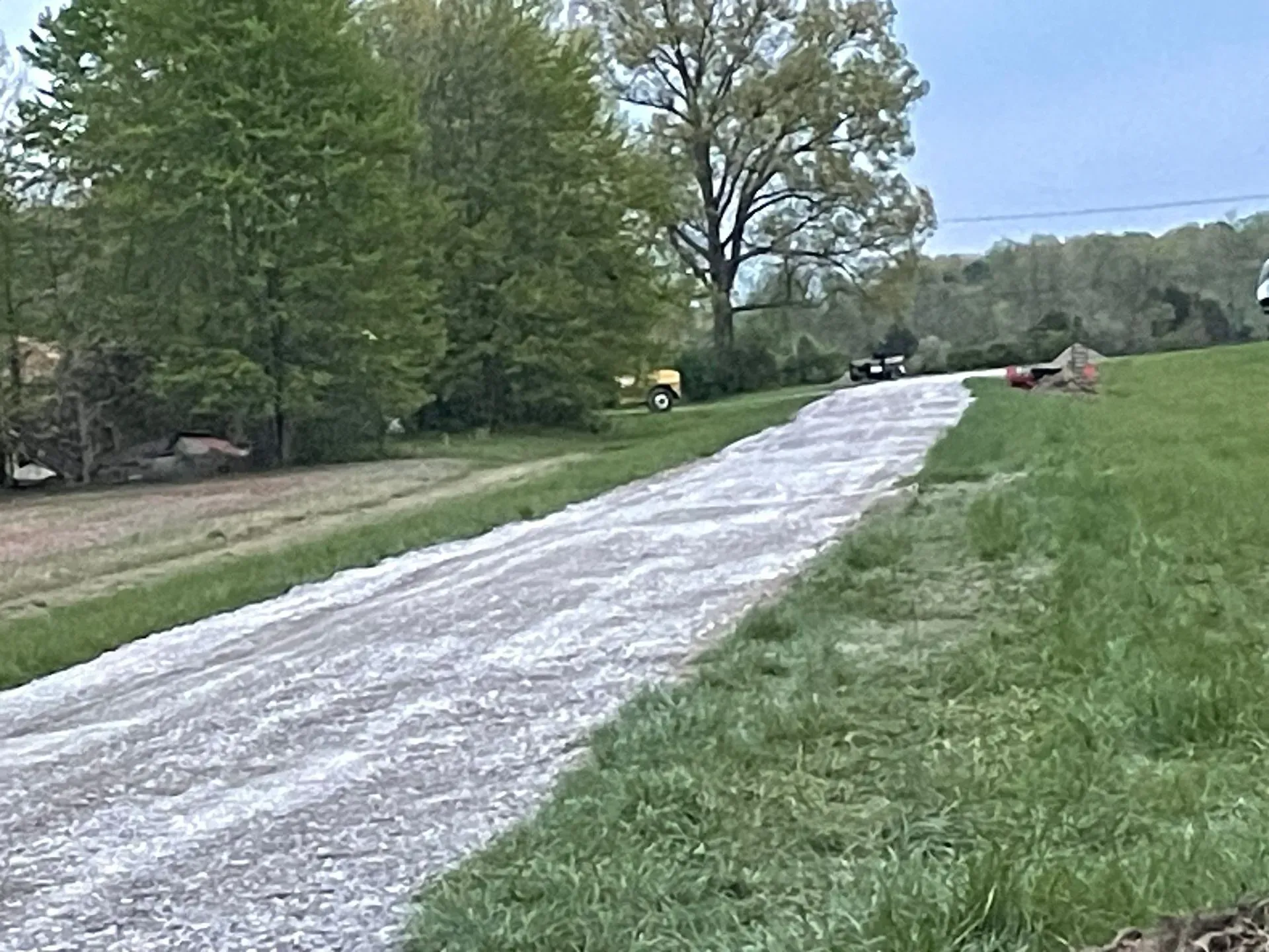 Gravel road through a grassy field with trees lining both sides under a cloudy sky
