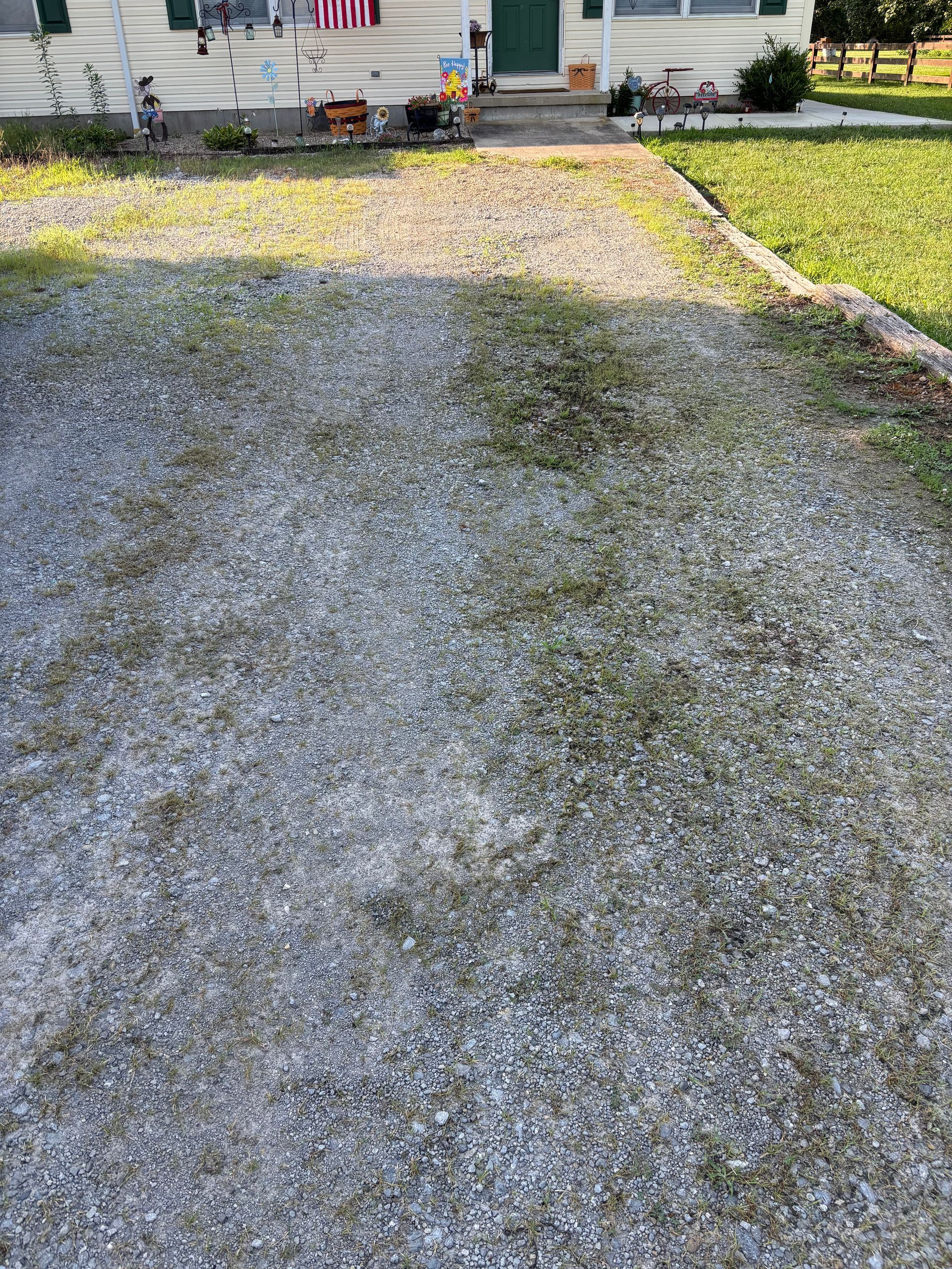 Gravel driveway leading to a house with a lawn and U.S. flag on the porch