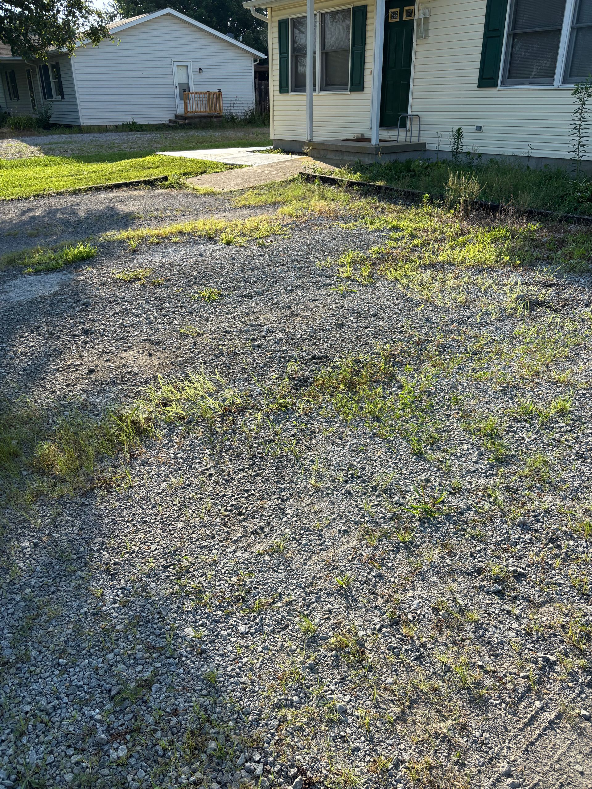 Gravel driveway beside a white house with a small concrete walkway and patchy grass