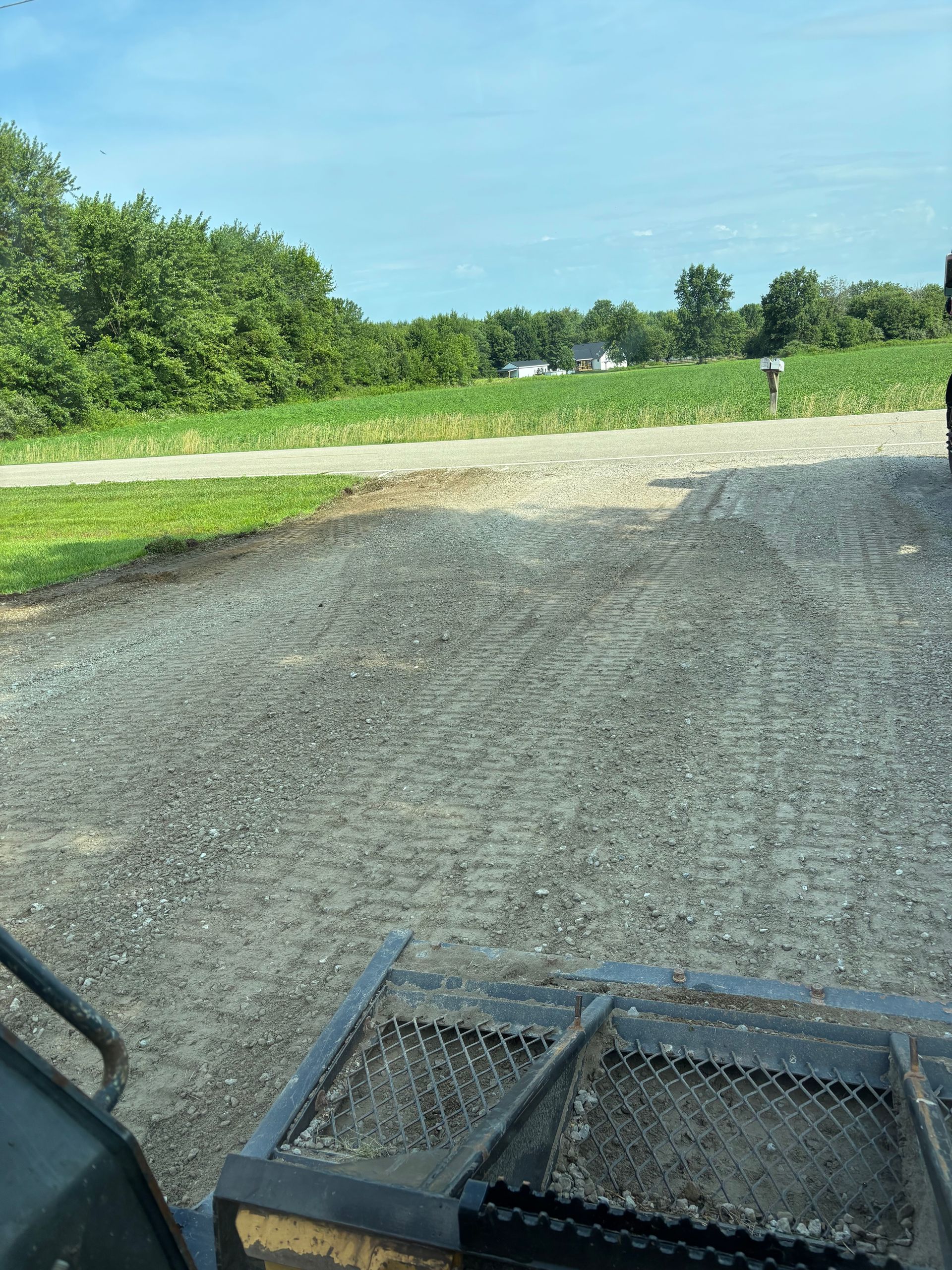 Gravel road with a dirt crossing, green trees at left, and a trailer edge in the foreground