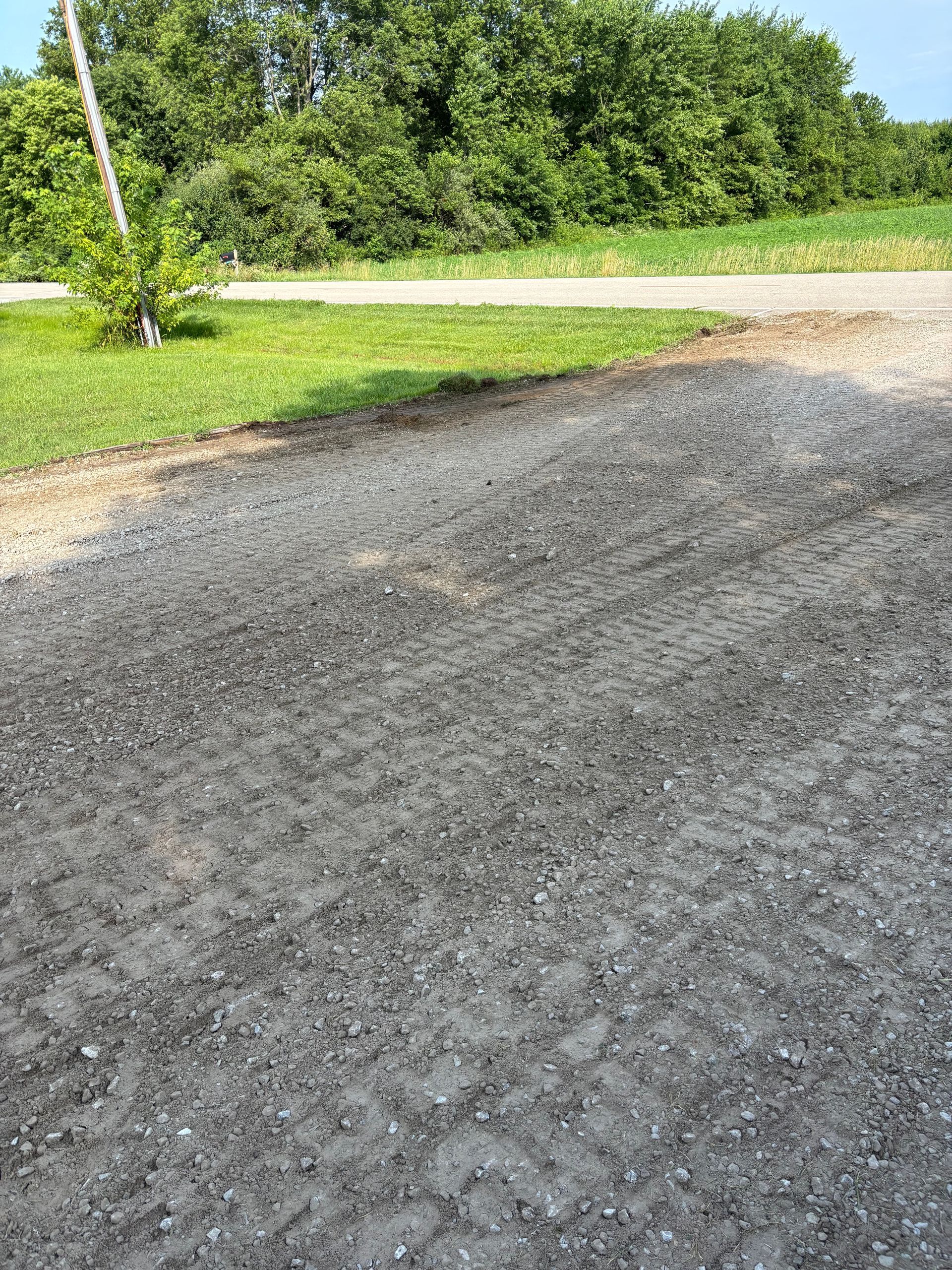 Freshly paved black asphalt driveway beside a grassy roadside and green trees