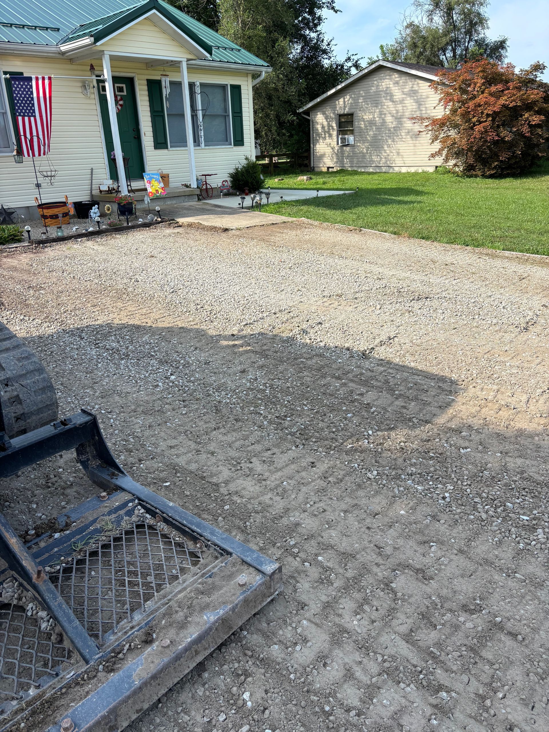 Gravel driveway beside a small white house with an American flag and detached garage on a sunny day