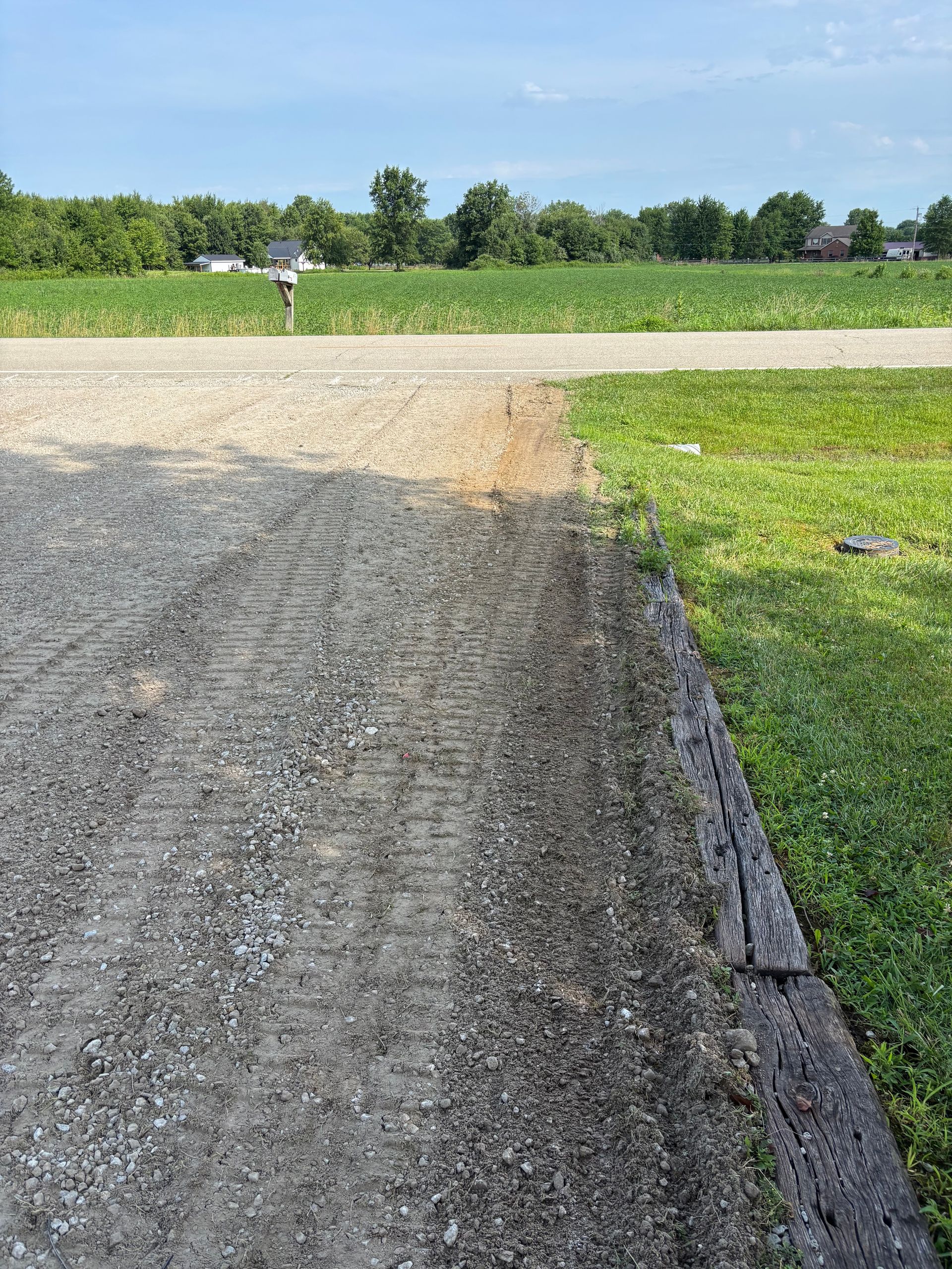 Gravel driveway leading to a paved road beside a green field under a blue sky