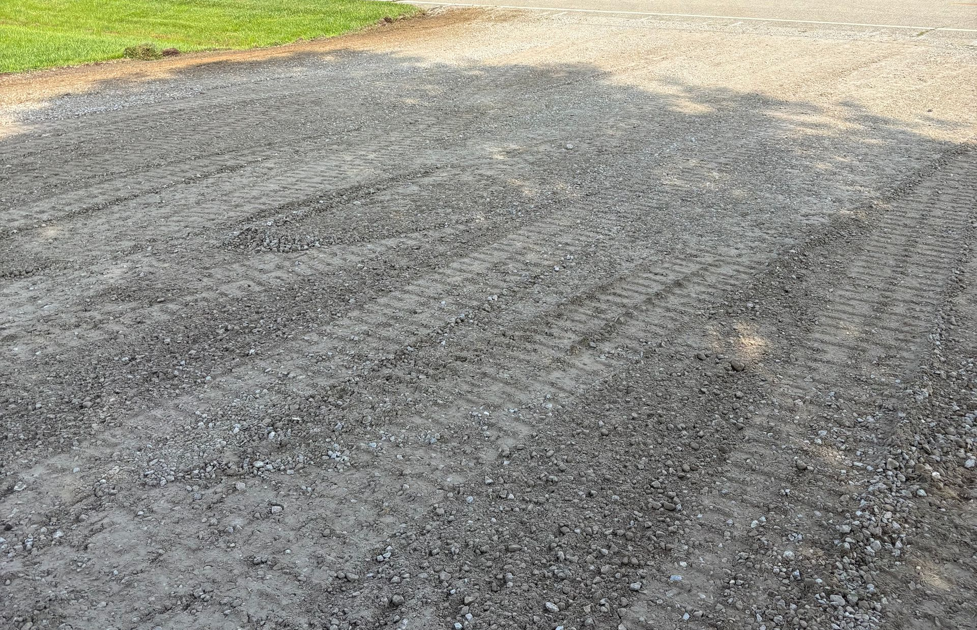 Gravel driveway with tire tracks beside a strip of green grass.