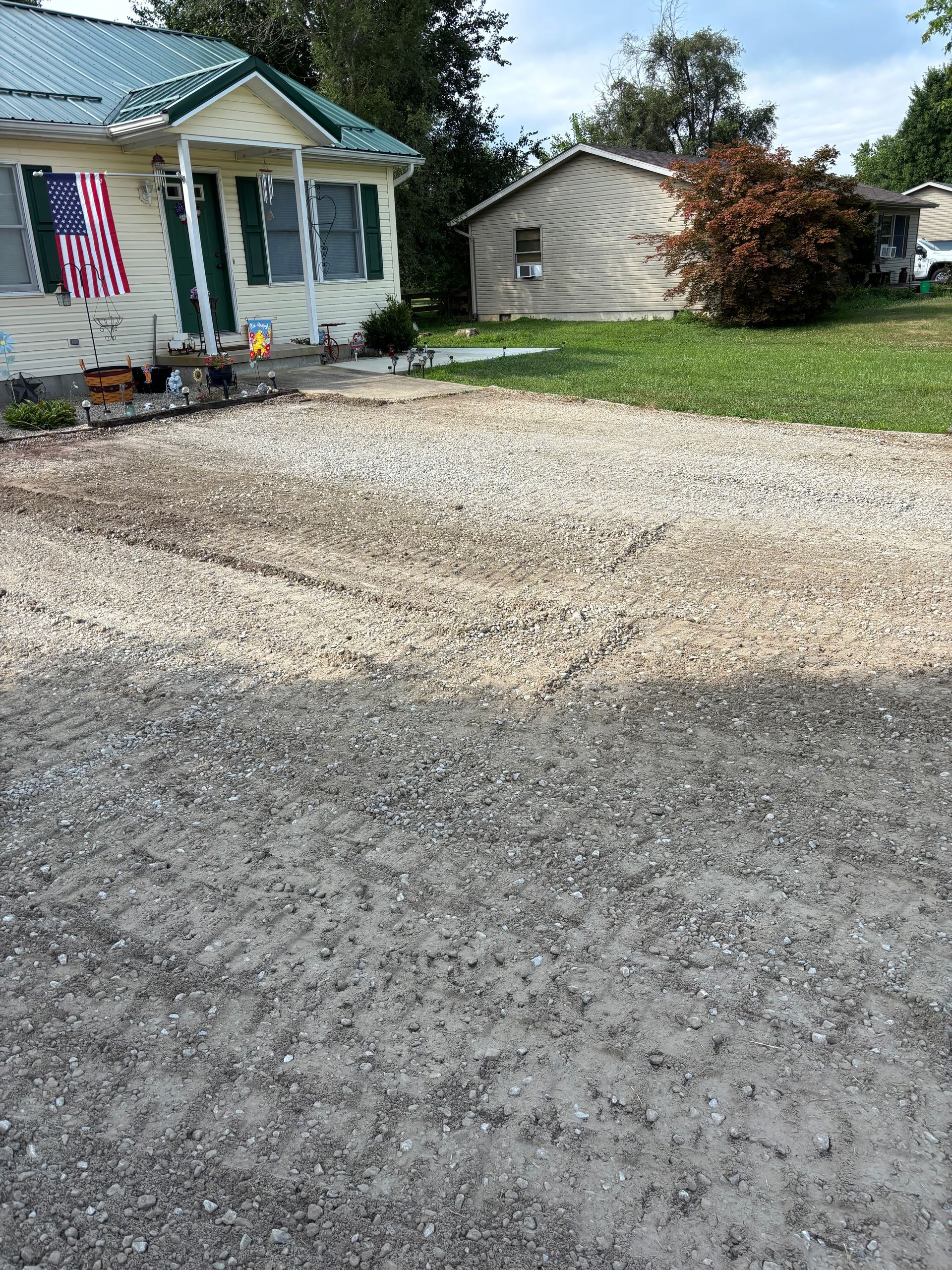 Gravel driveway beside a small house with an American flag and a garage in the background.