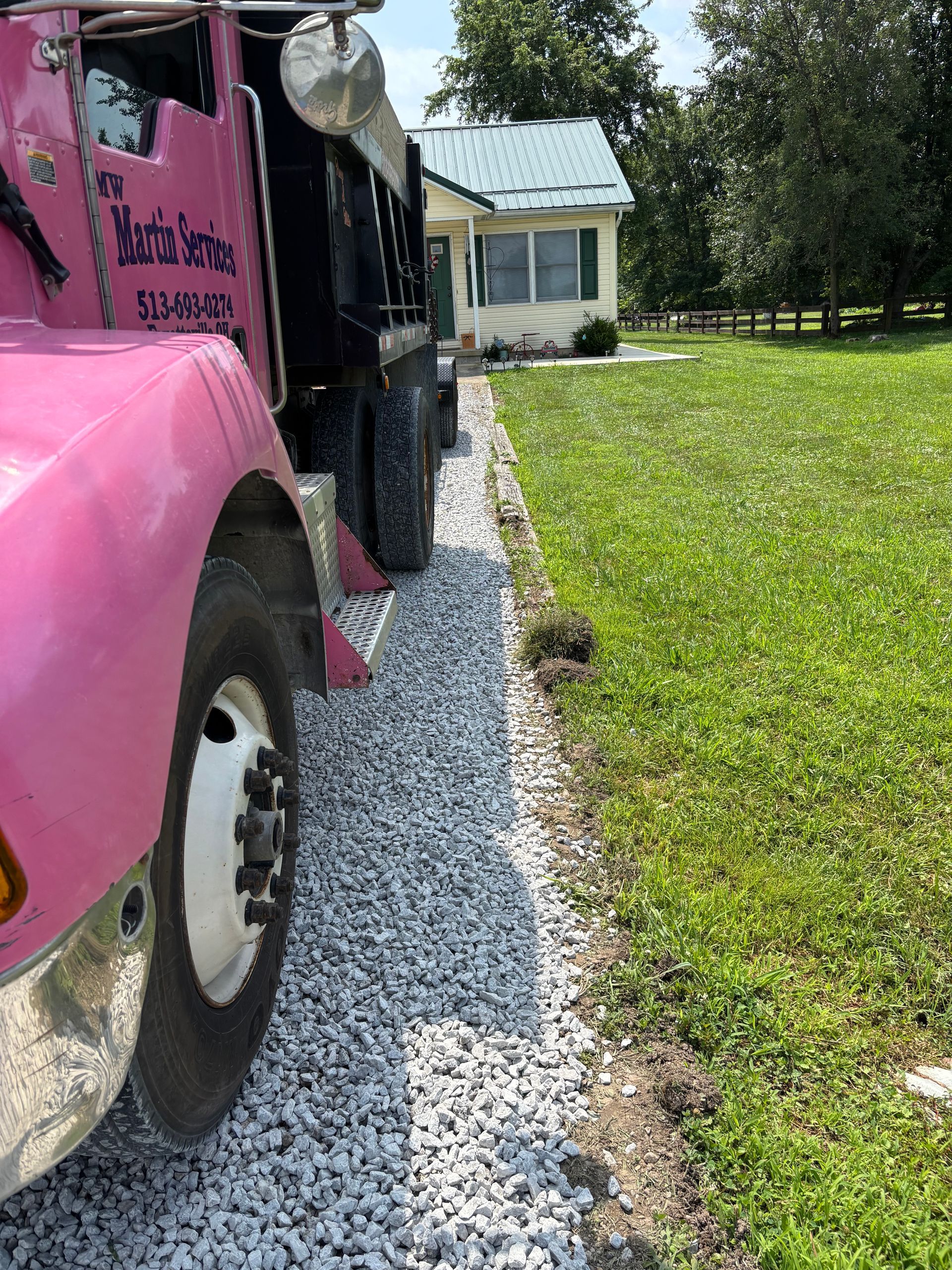Pink truck parked beside a gravel driveway with a grassy lawn and house in the background