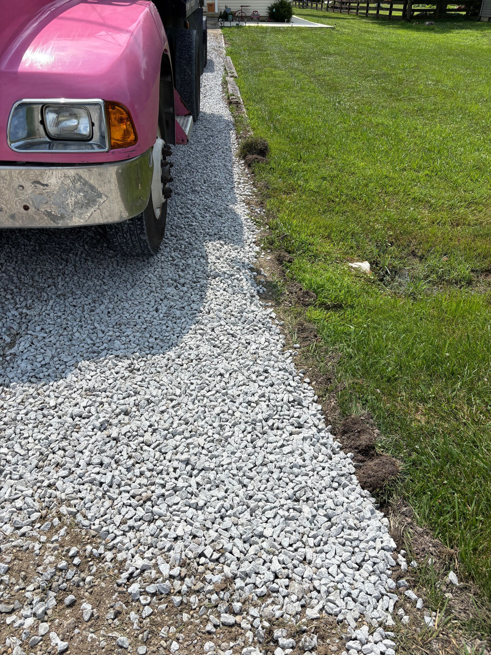Pink truck parked beside a fresh gravel driveway edge next to green grass.