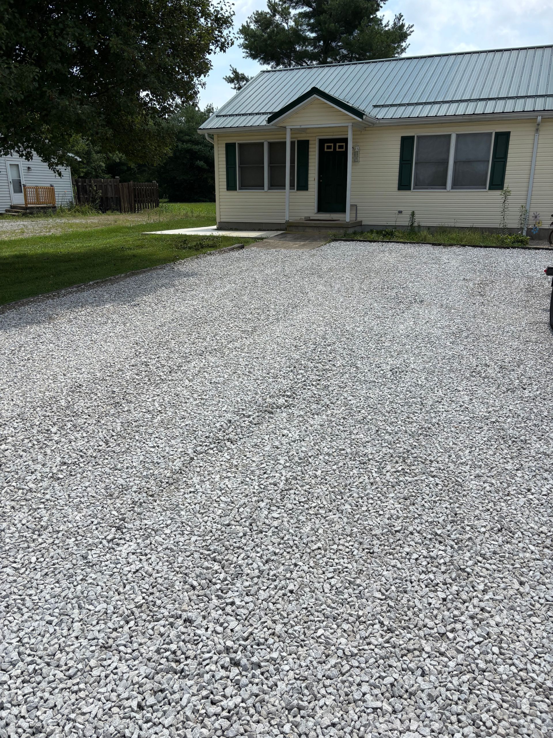 Small beige house with a metal roof and a large gravel driveway in front