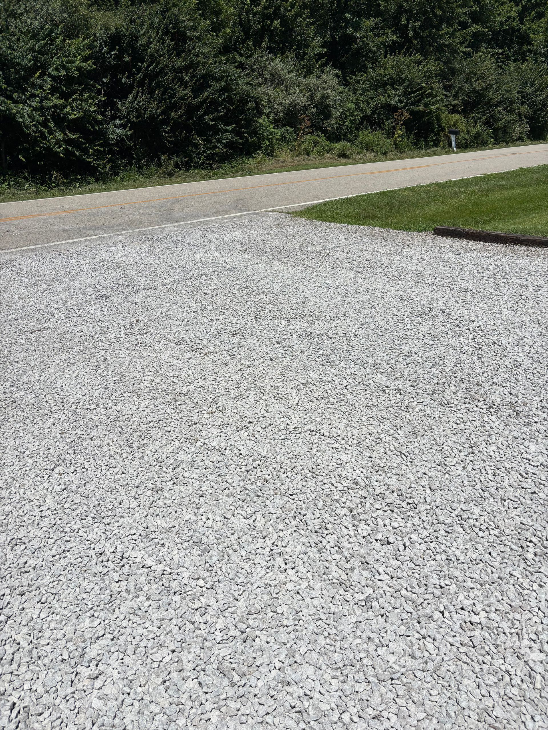 Gravel driveway curving beside a grassy lawn with trees in the background.
