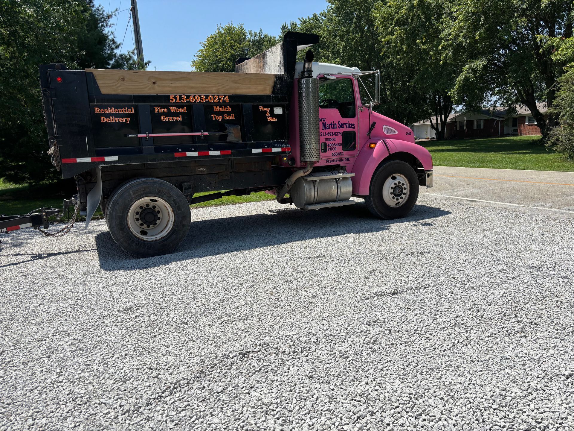 Pink-and-black dump truck parked on a gravel road in a sunny rural area