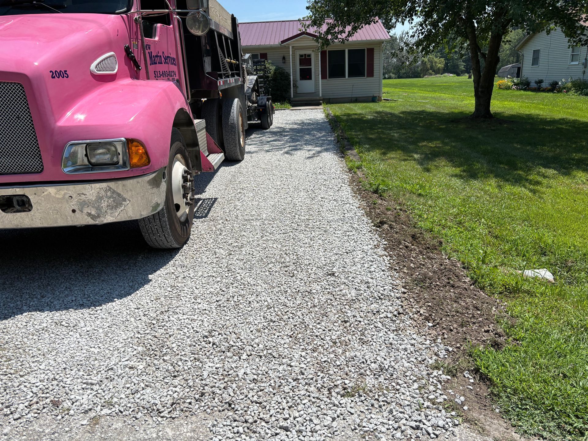 Pink truck parked on a gravel driveway beside a grassy yard and a small house
