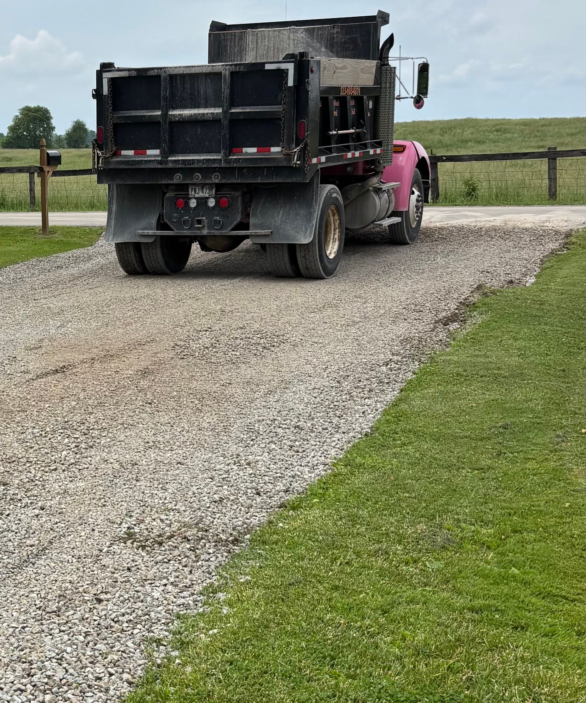 Dump truck on a gravel driveway beside a grassy field under a cloudy sky