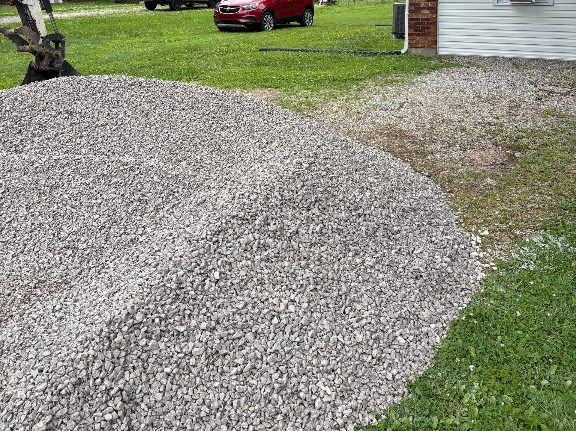 Large gravel driveway beside a grassy yard, with a red car parked in the background.