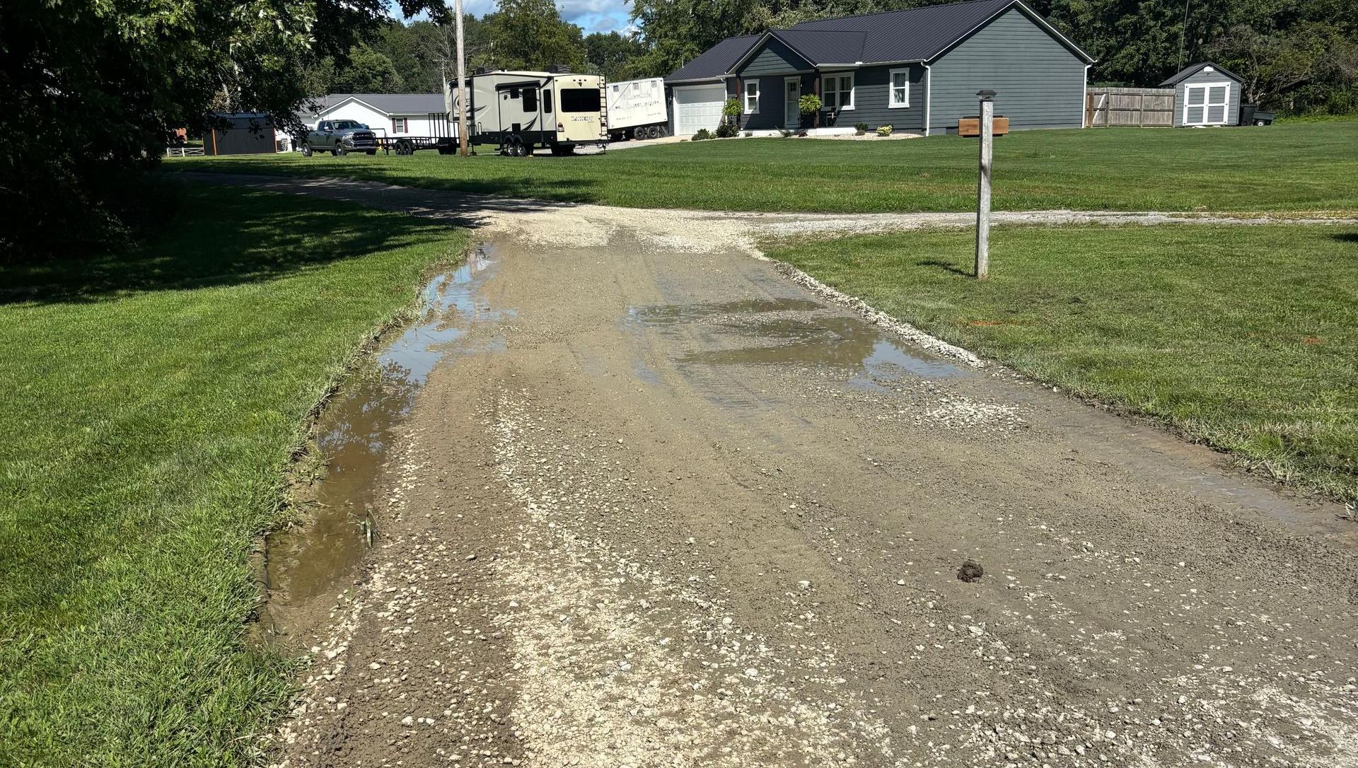Gravel driveway washed out by flooding, with muddy water 