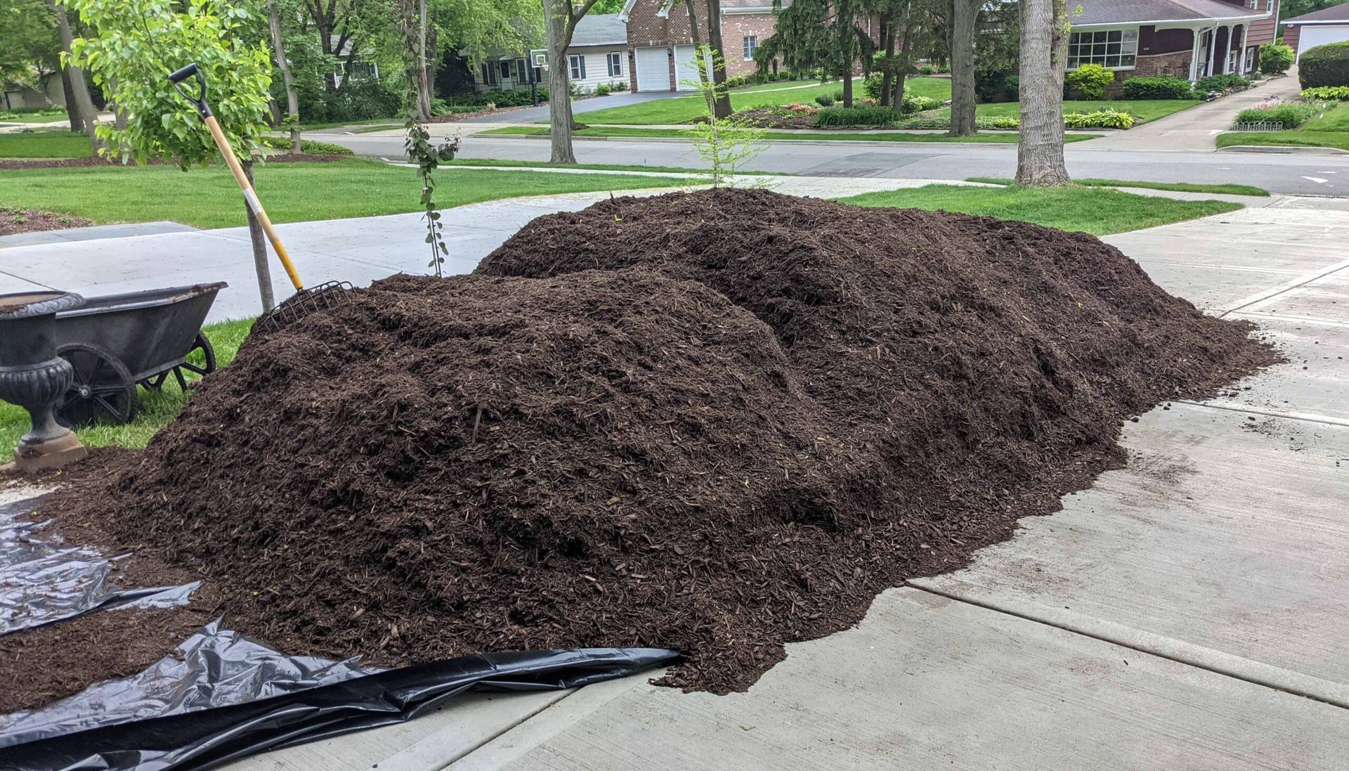 Large pile of dark mulch on a driveway beside a yard and street