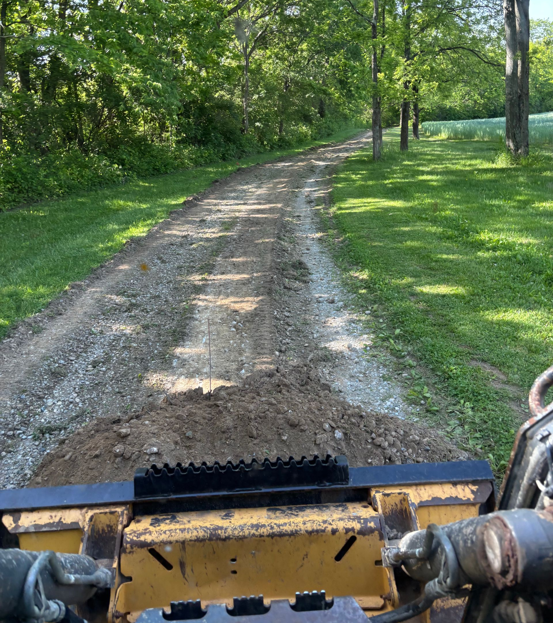 View from a tractor driving on a gravel path through a green, wooded yard