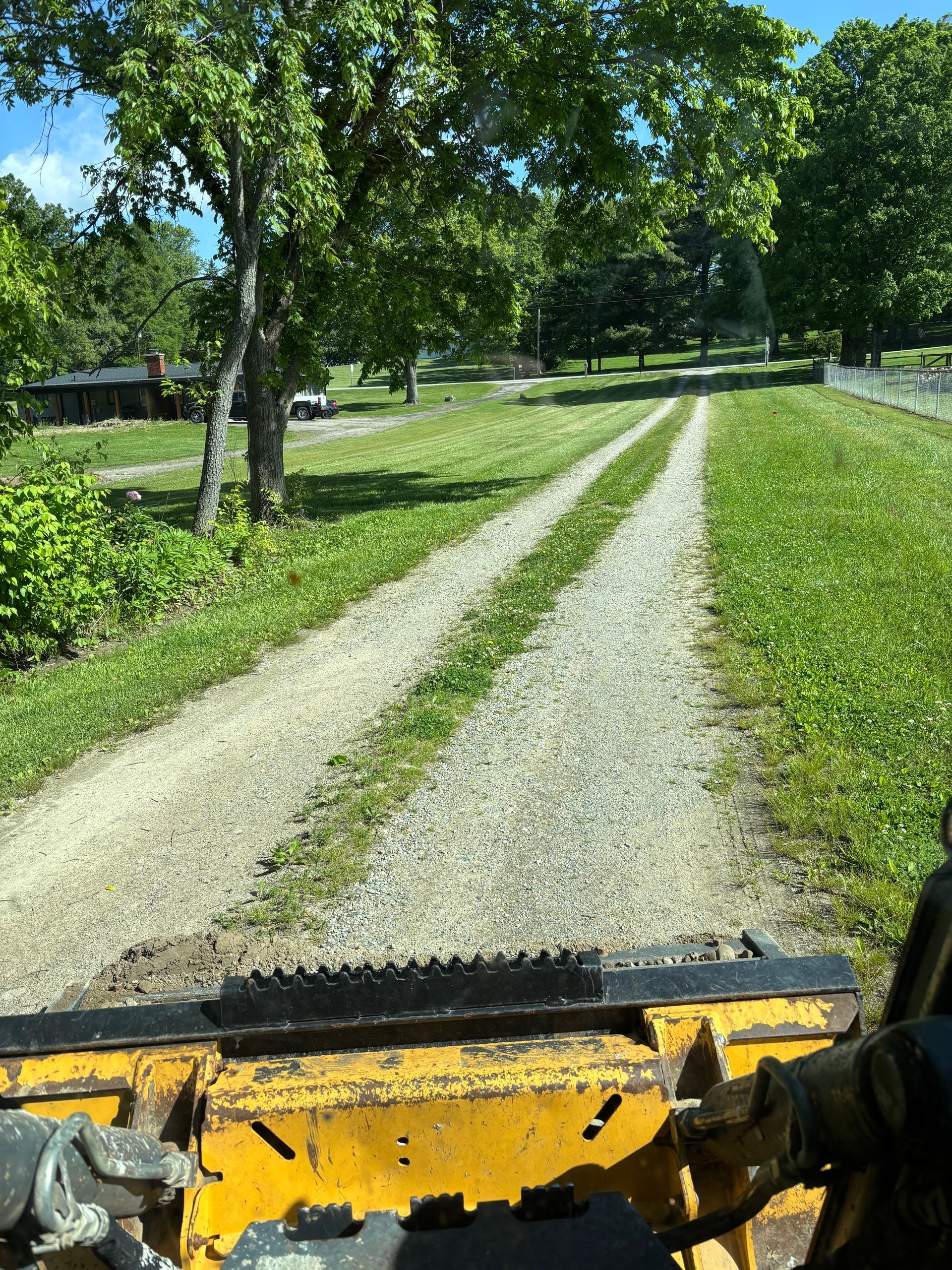 View from a yellow utility vehicle driving on a gravel lane through a green park