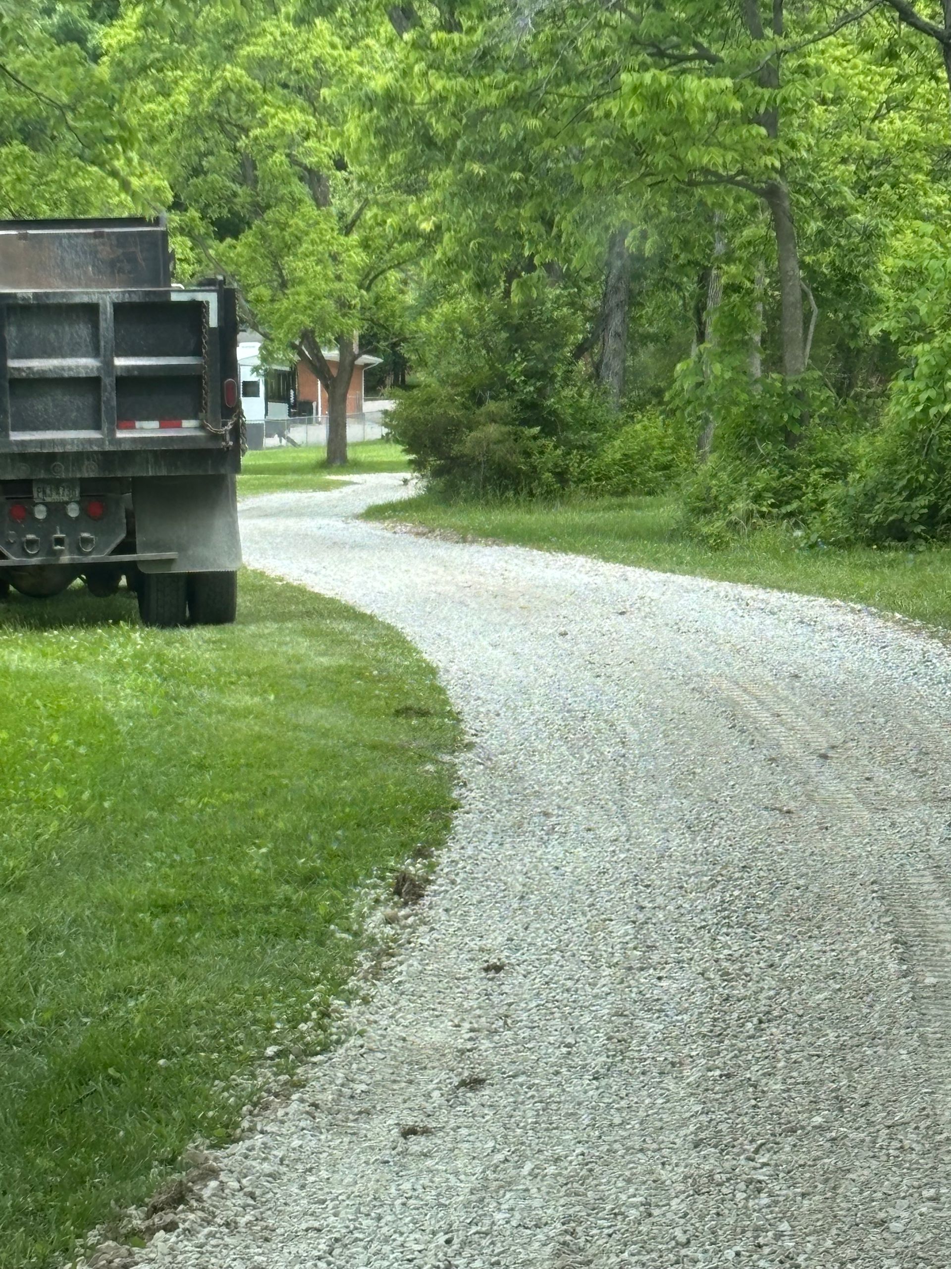 Gravel road curving through a green wooded area beside a parked dump truck