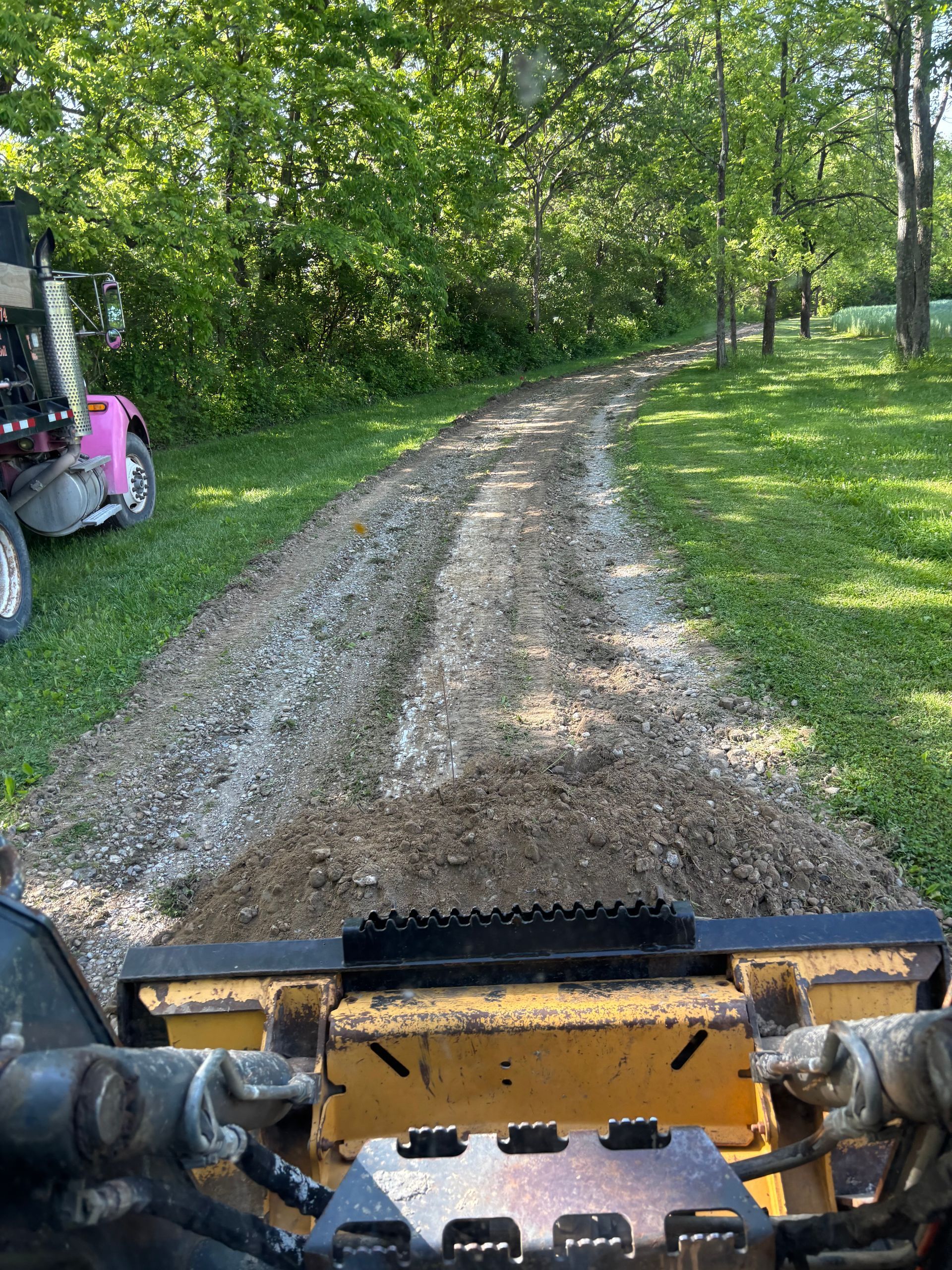 View from a construction machine on a muddy gravel path through a green wooded area