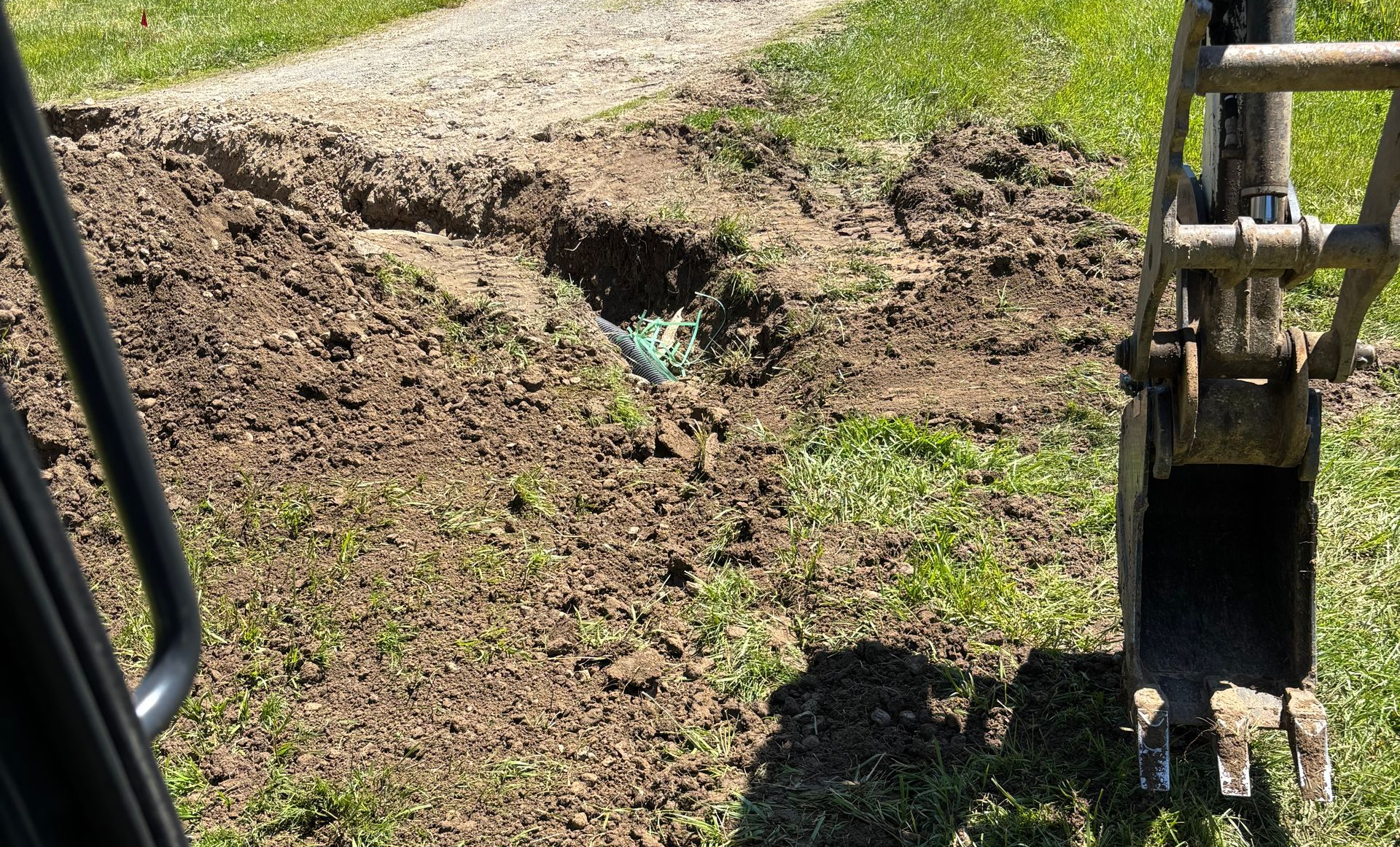 Excavator bucket digging a dirt trench beside a grassy path