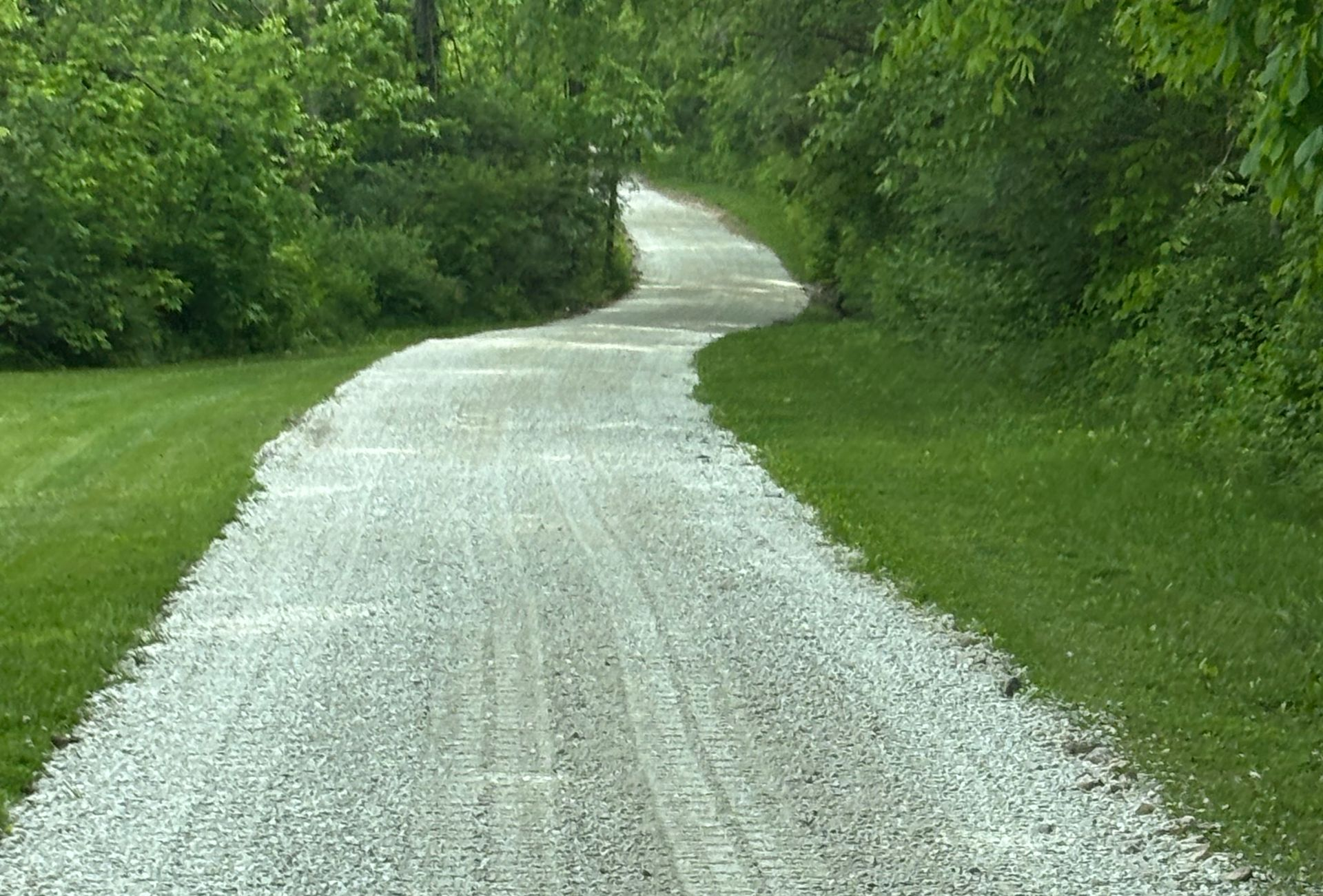 Gravel path winding through lush green trees and grass on a cloudy day