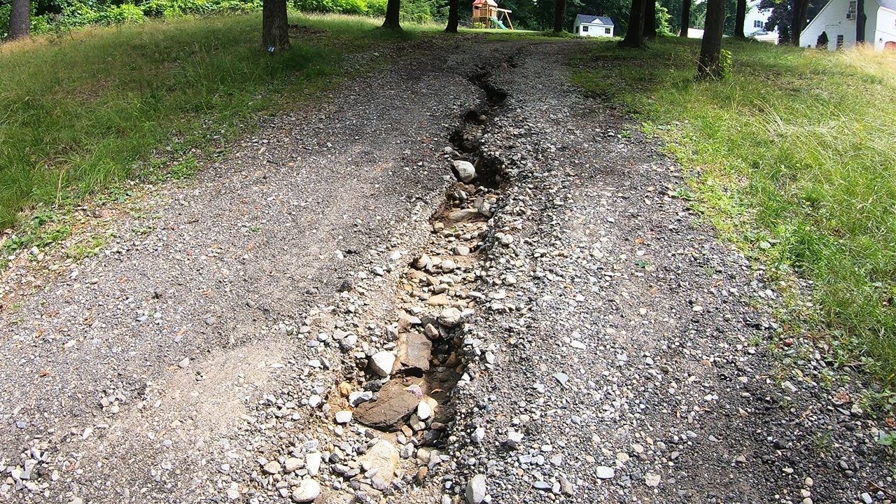 Cracked gravel driveway with a deep eroded trench running down the center.