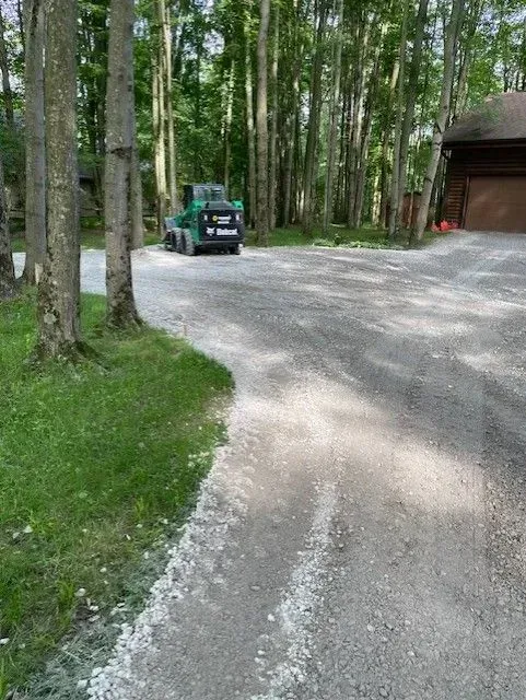 Green off-road vehicle on a gravel driveway beside tall trees and a garage.