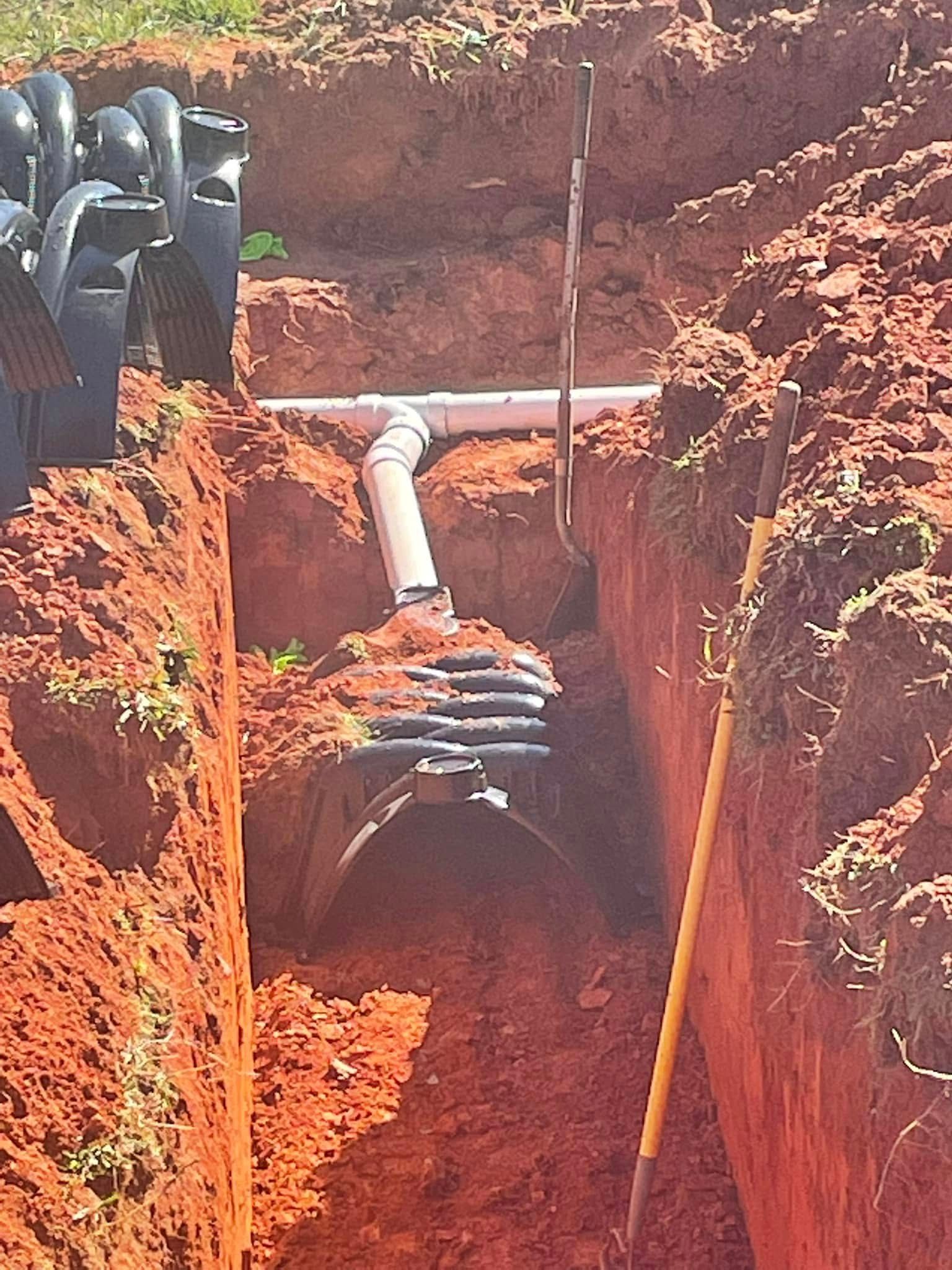 Construction site with a septic tank and pipes in a trench. Red soil, black tank, and white PVC.