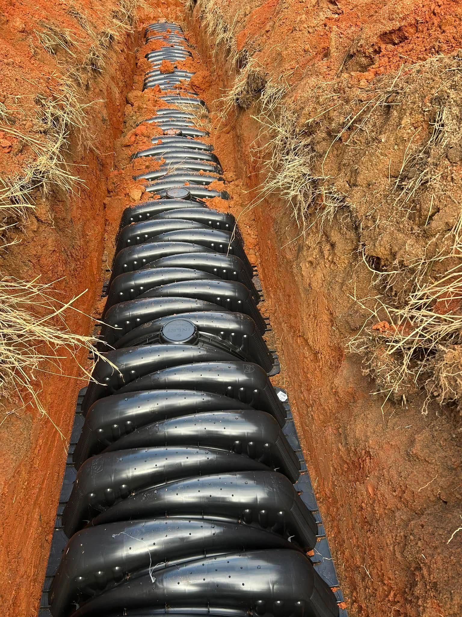 Black drainage system installed in a trench, surrounded by reddish-brown soil.