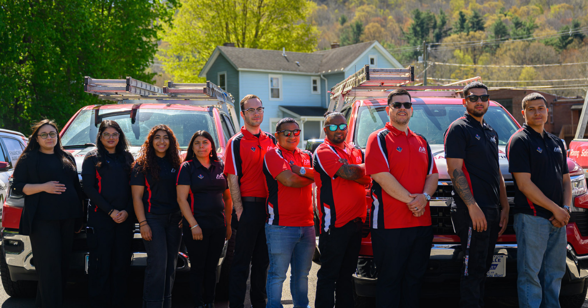 Group of people in red and black shirts posing outdoors in front of SUVs and a house