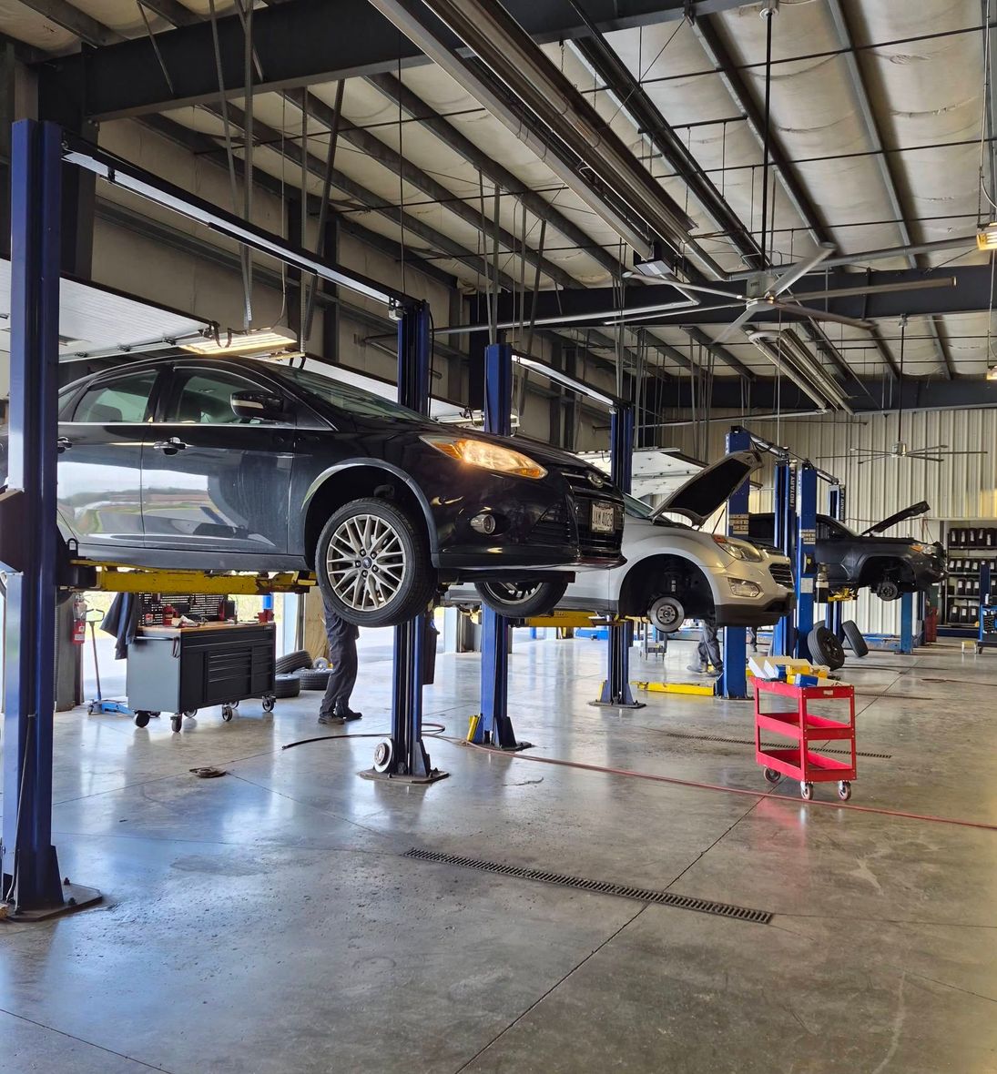 Cars on lifts inside an auto repair shop with a mechanic working nearby | Westside Tire & Service