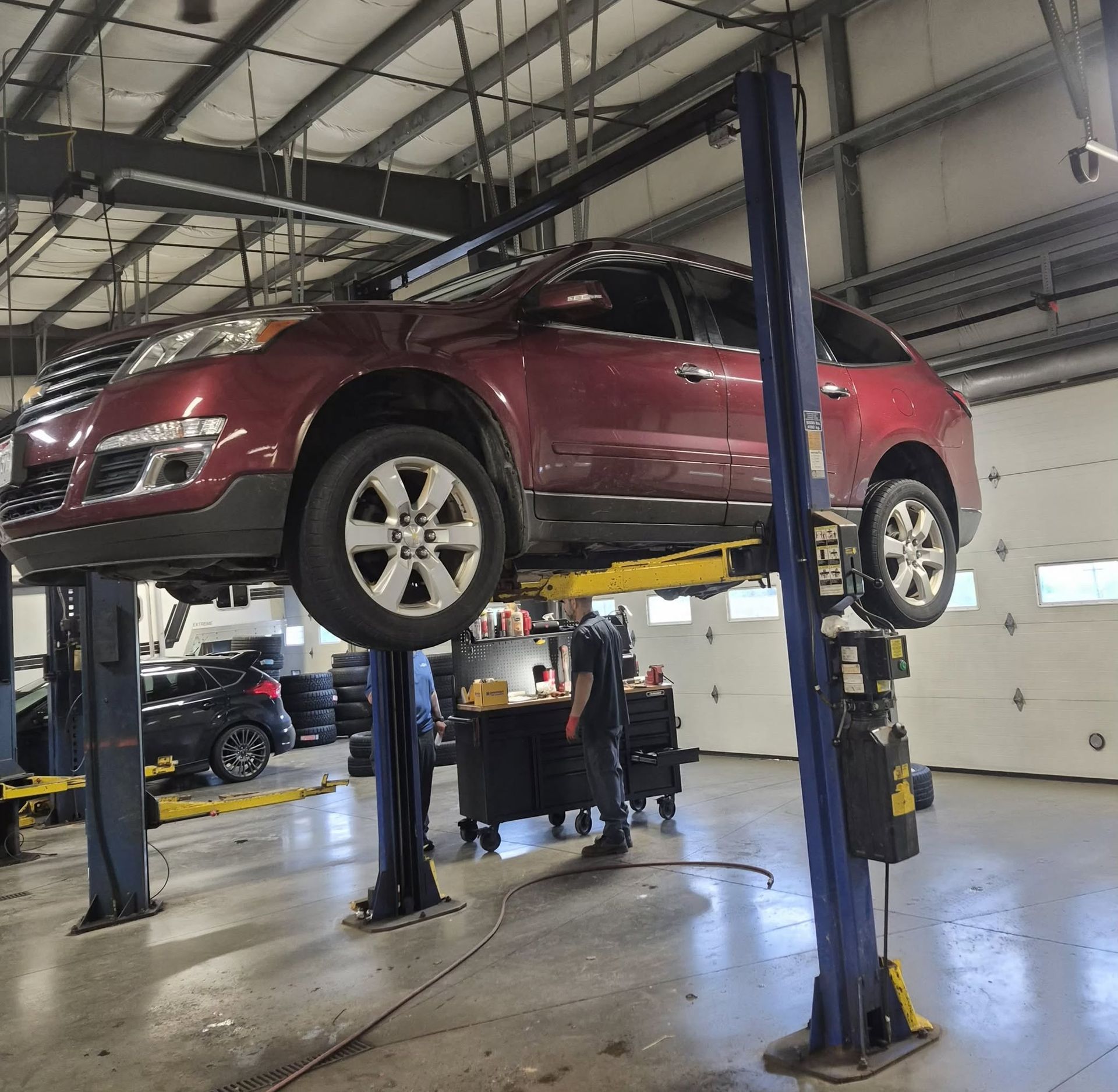 Red SUV on a four-post lift in an auto repair shop, with mechanics working below | Westside Tire & Service