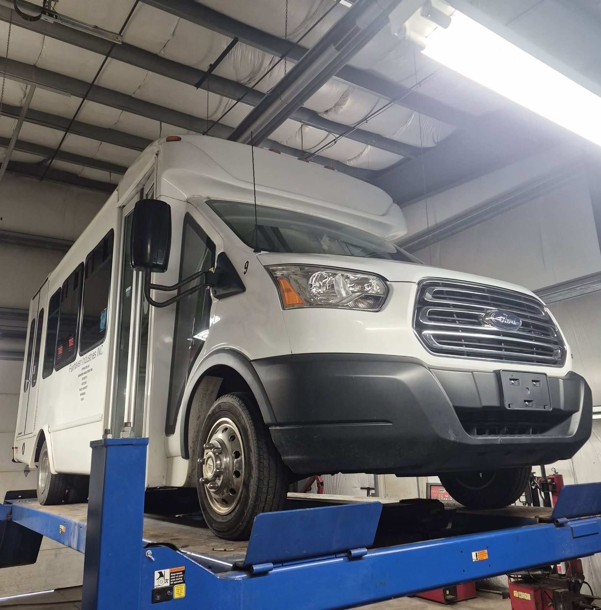 White shuttle bus on a blue lift in an indoor auto garage | Westside Tire & Service