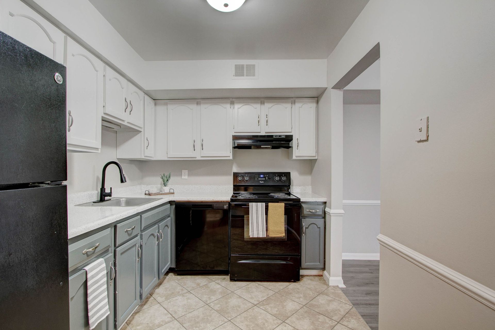 Kitchen with white upper cabinets, gray lower cabinets, black appliances and a neutral-colored floor.