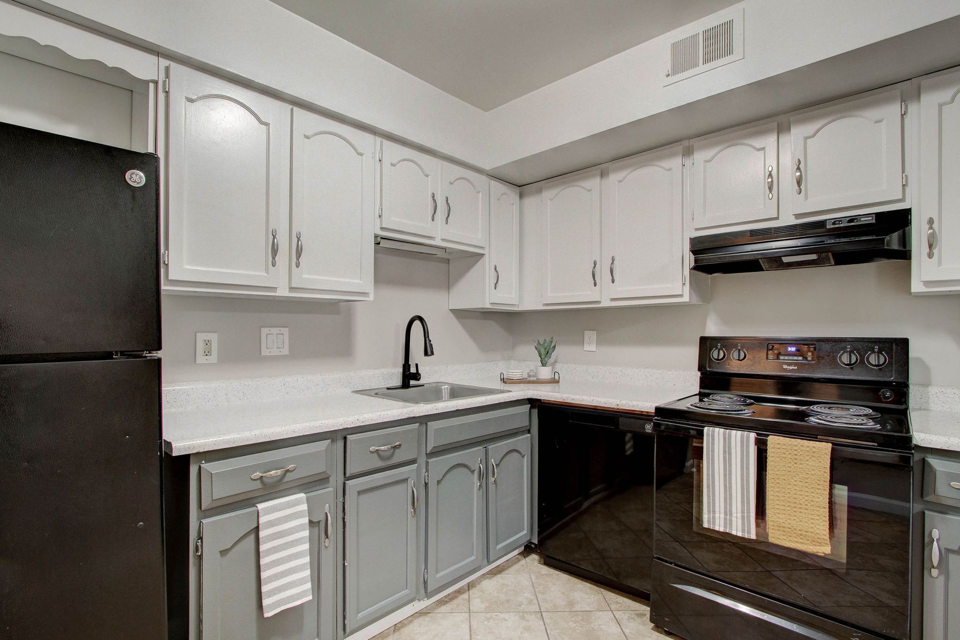 Kitchen with gray and white cabinets, black appliances, and white countertops.