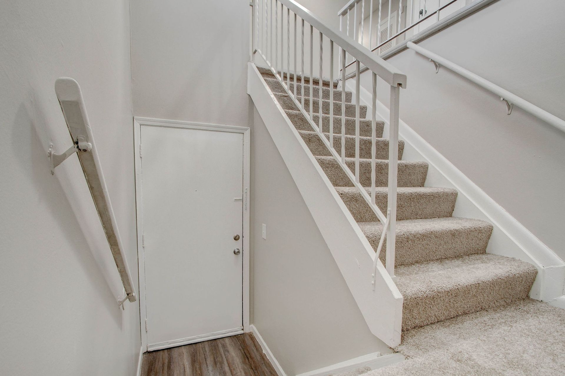 Staircase with beige carpet and white railing, leading to a second floor; door and angled wall-mounted items.