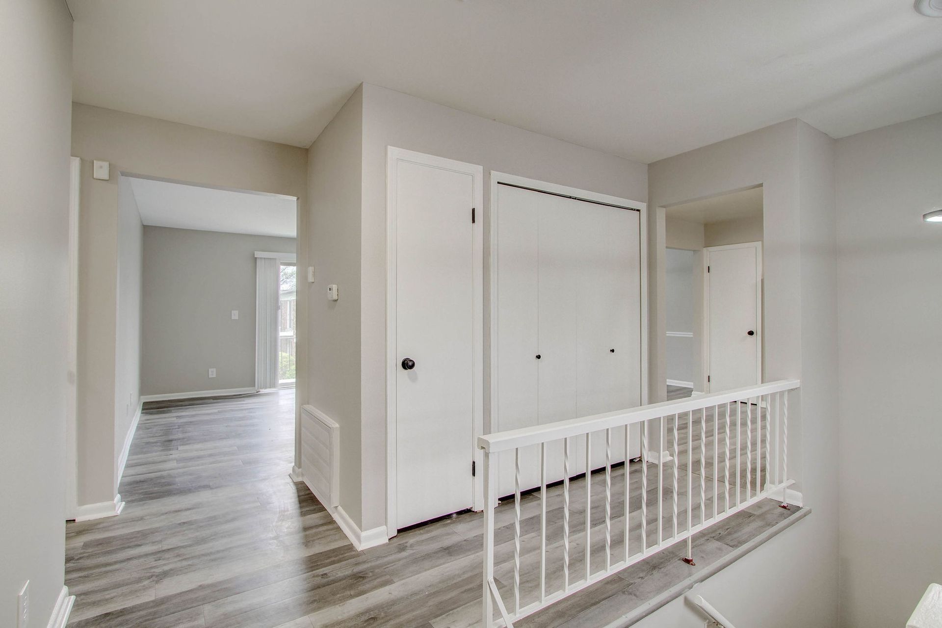 Interior hallway with white railing, doors, and light gray walls and flooring.
